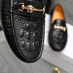 Black leather loafer close-up with embossed texture and gold-tone decorative buckle strap.
