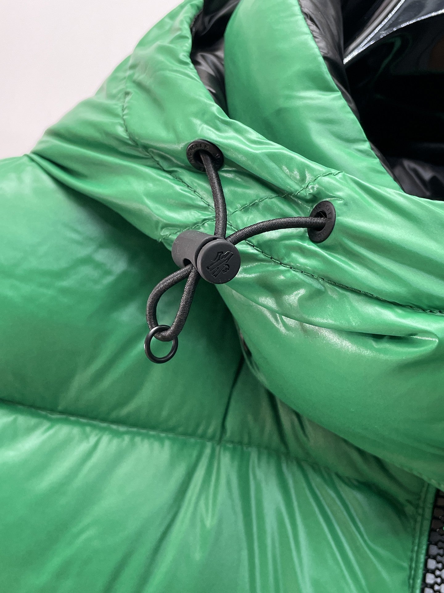 Green puffer vest hood with black drawstring cords and round toggle detail