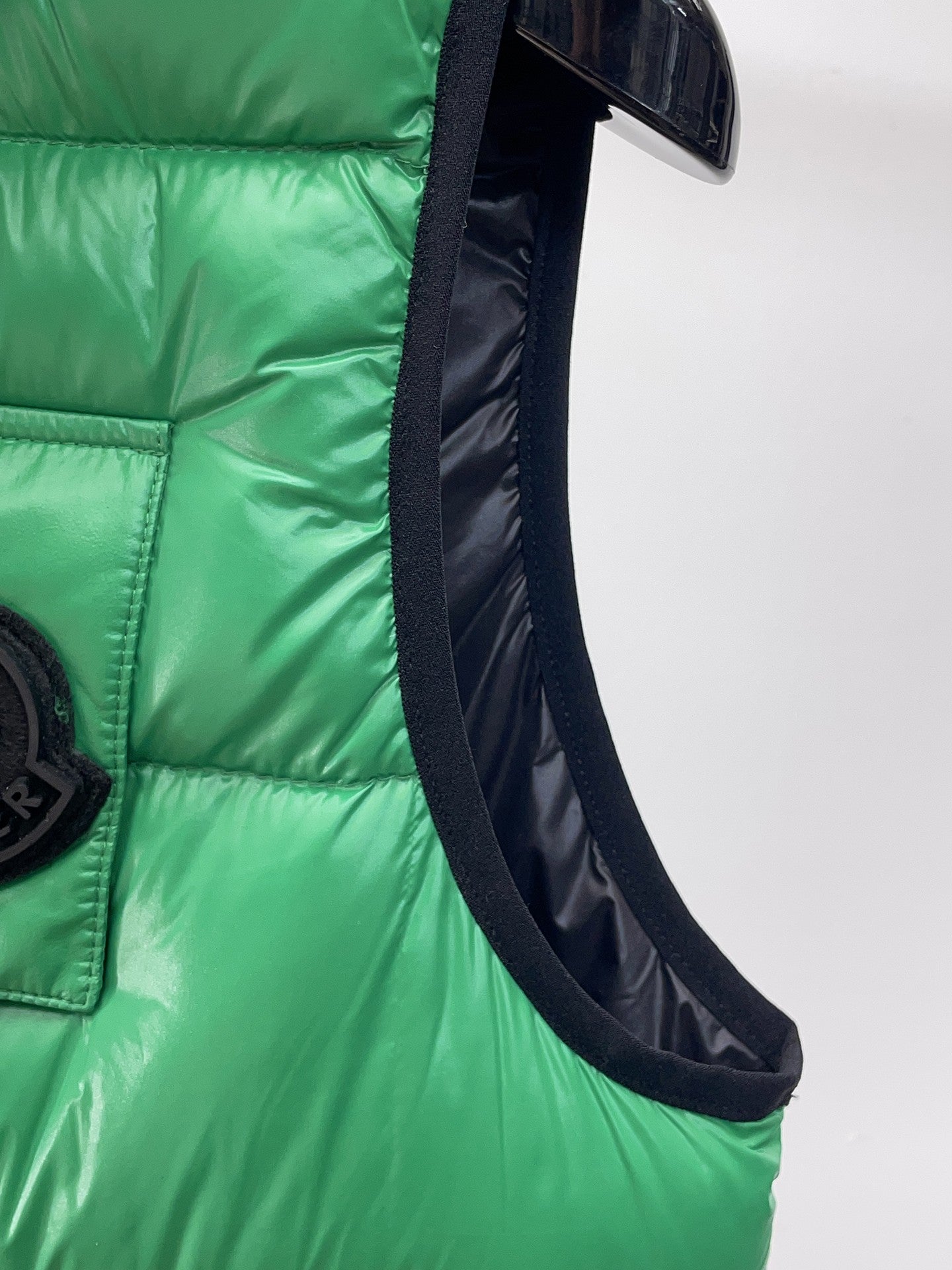 Green puffer vest side view with black-trimmed arm opening and pocket edge