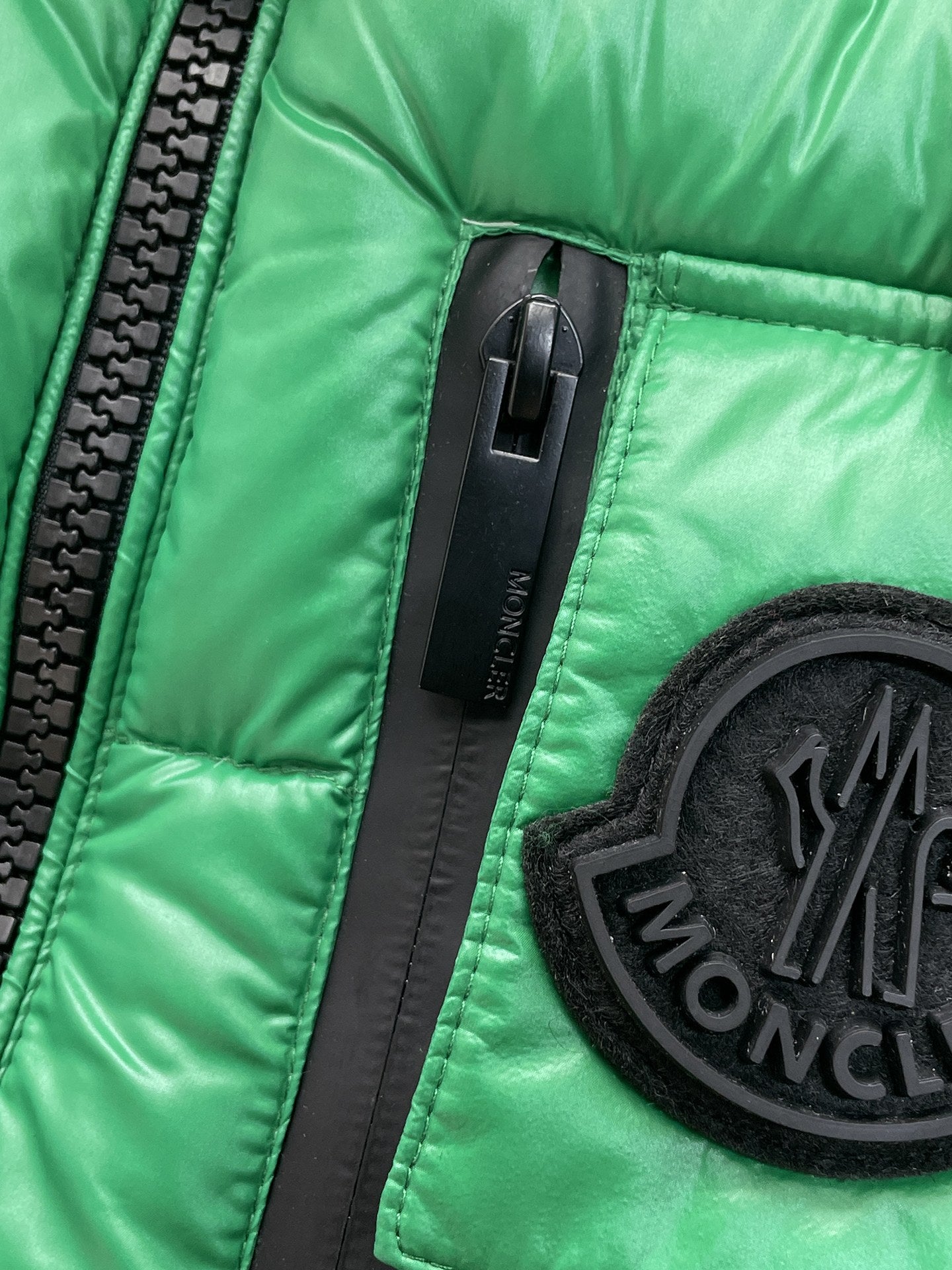 Green puffer vest close-up of zipper and black circular Moncler logo patch