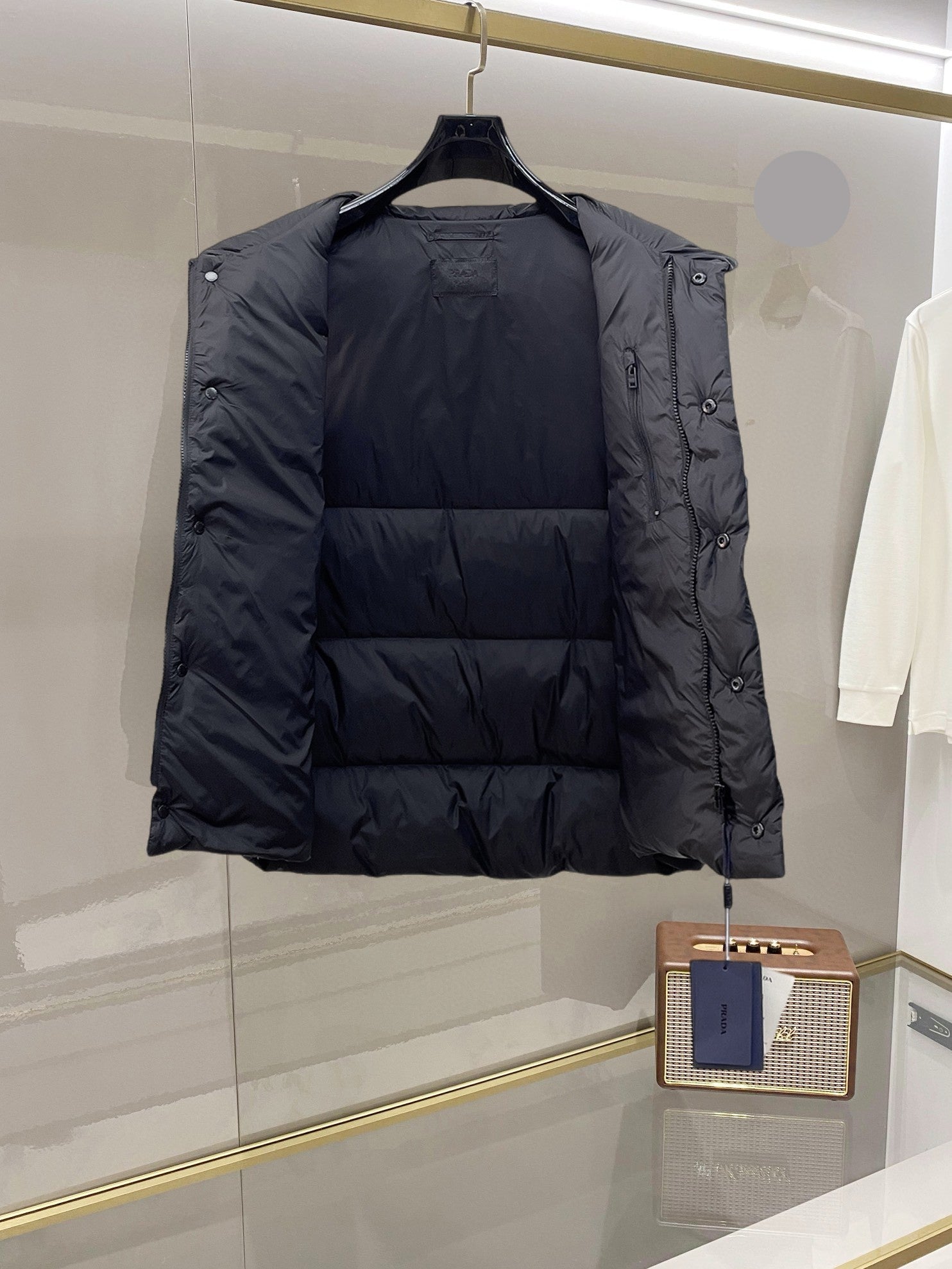 Dark long puffer vest with open side and buttoned strap at the armhole