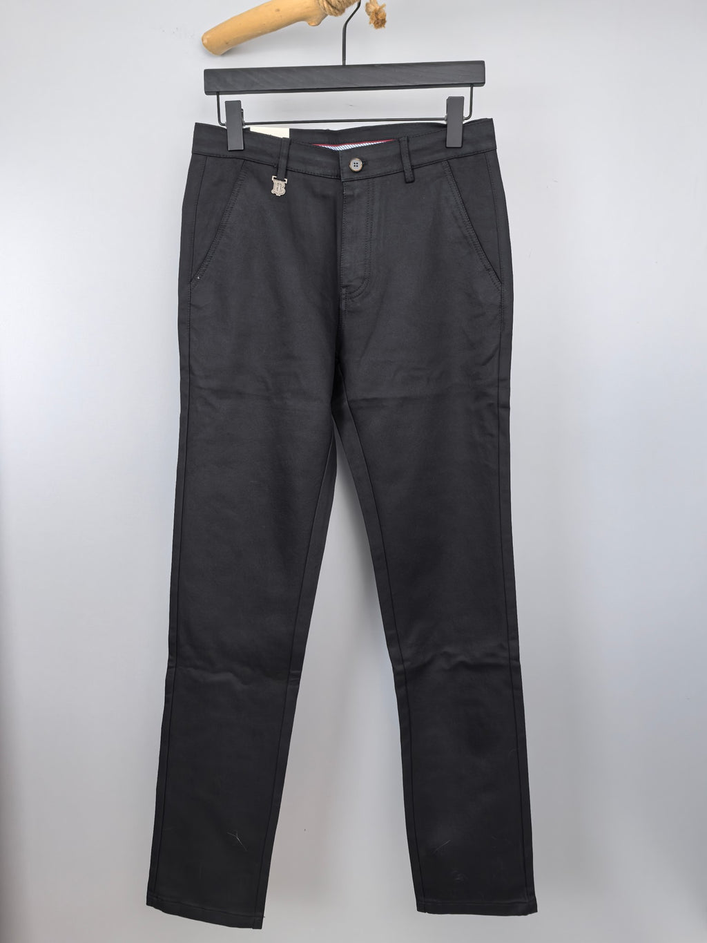 Black Burberry trousers on hanger, front view with belt loops and button closure