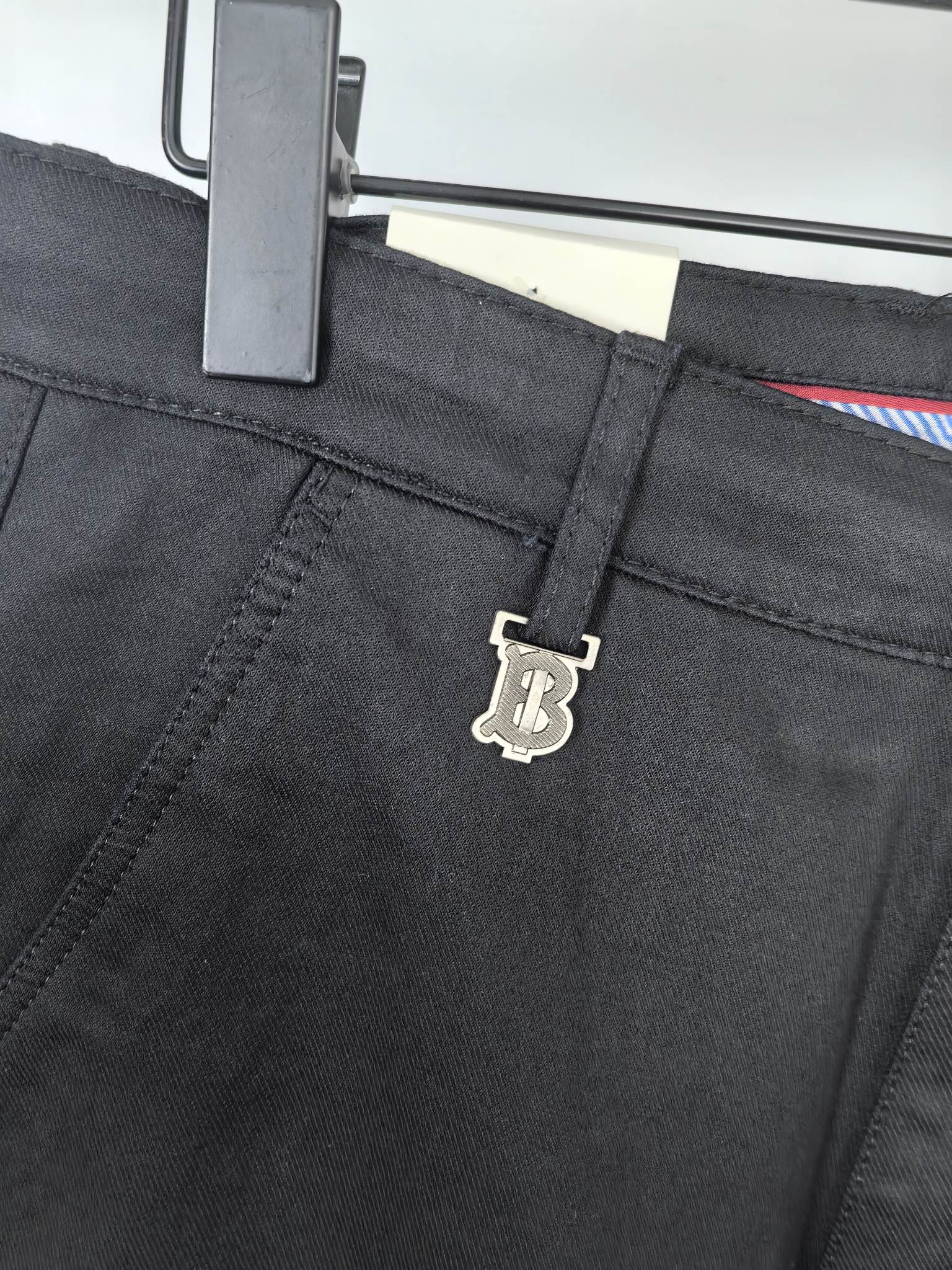 Black Burberry trouser waistband with logo charm on the adjustment strap