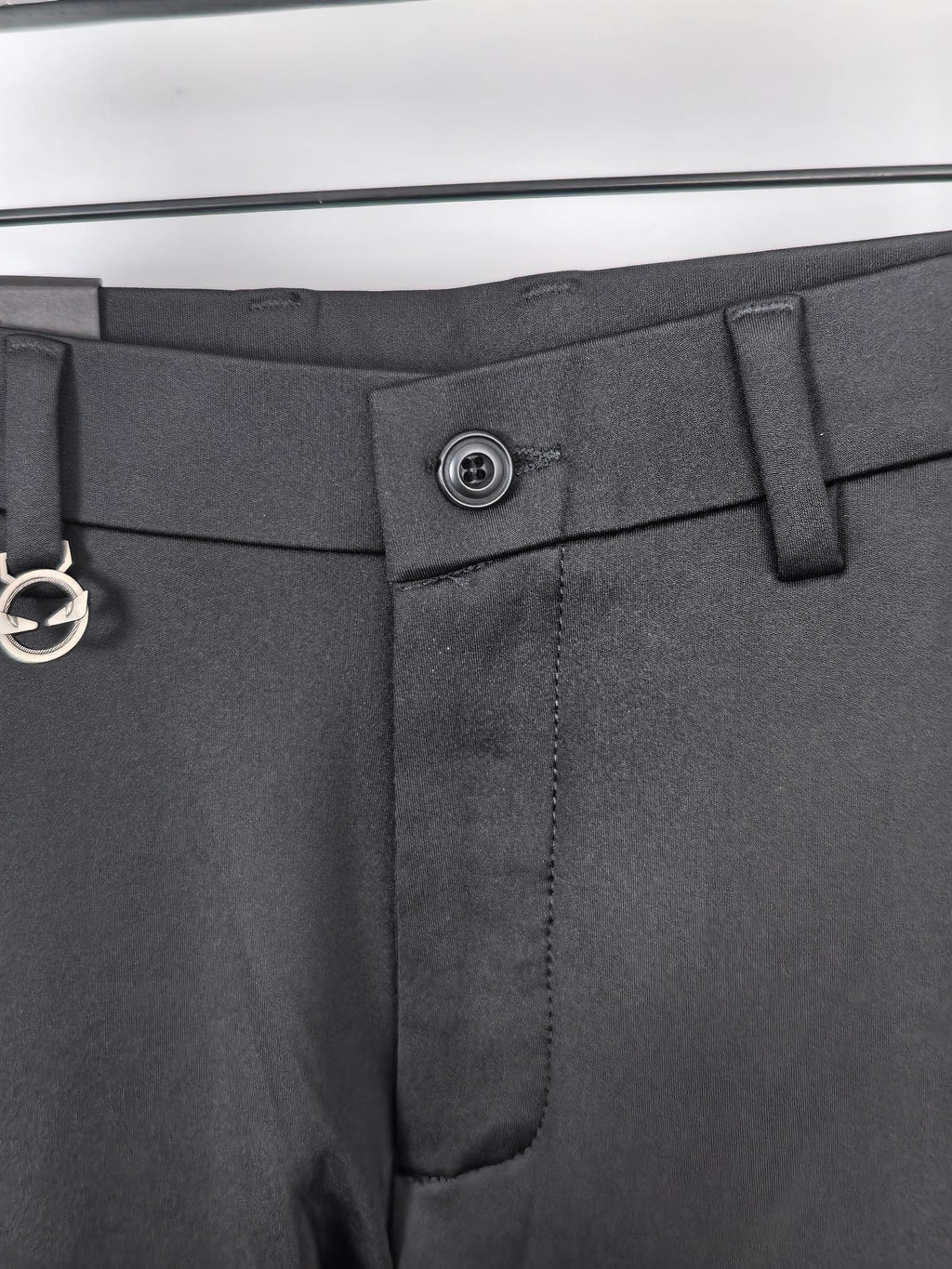 Waistband close-up with metal button and belt loop on black trousers