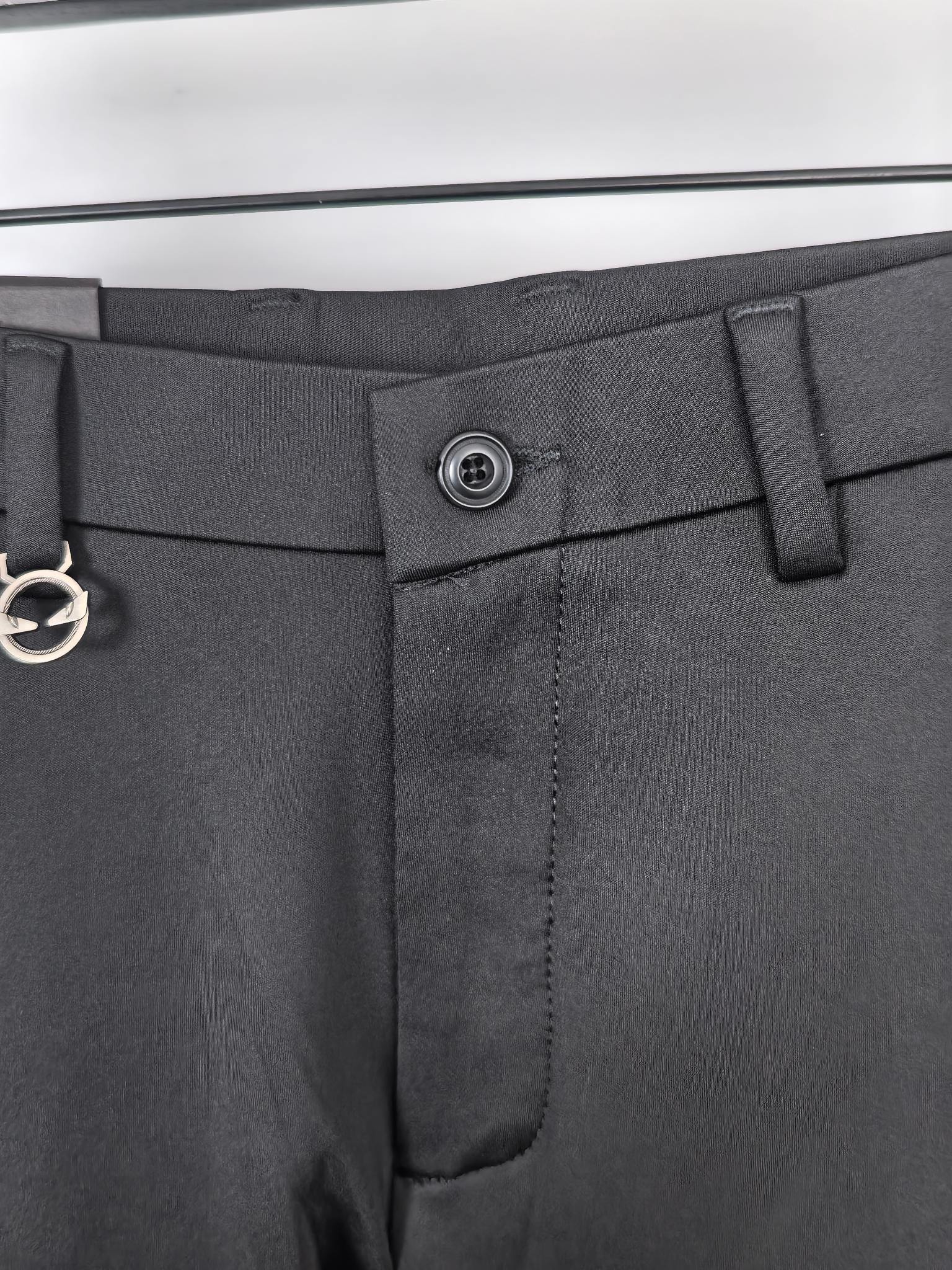Waistband close-up with metal button and belt loop on black trousers