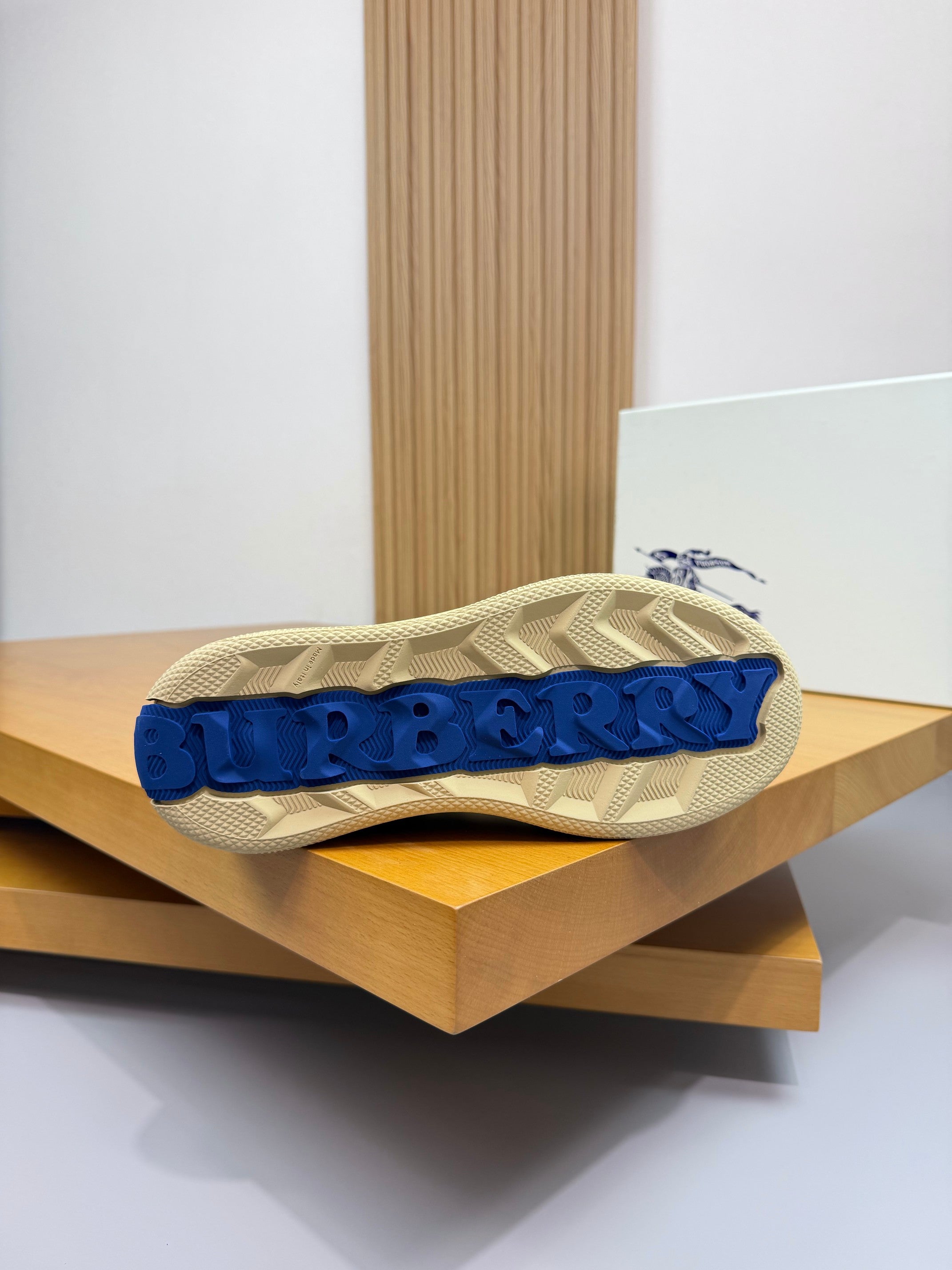 Burberry low-top sneaker sole view with blue tread lettering and beige upper