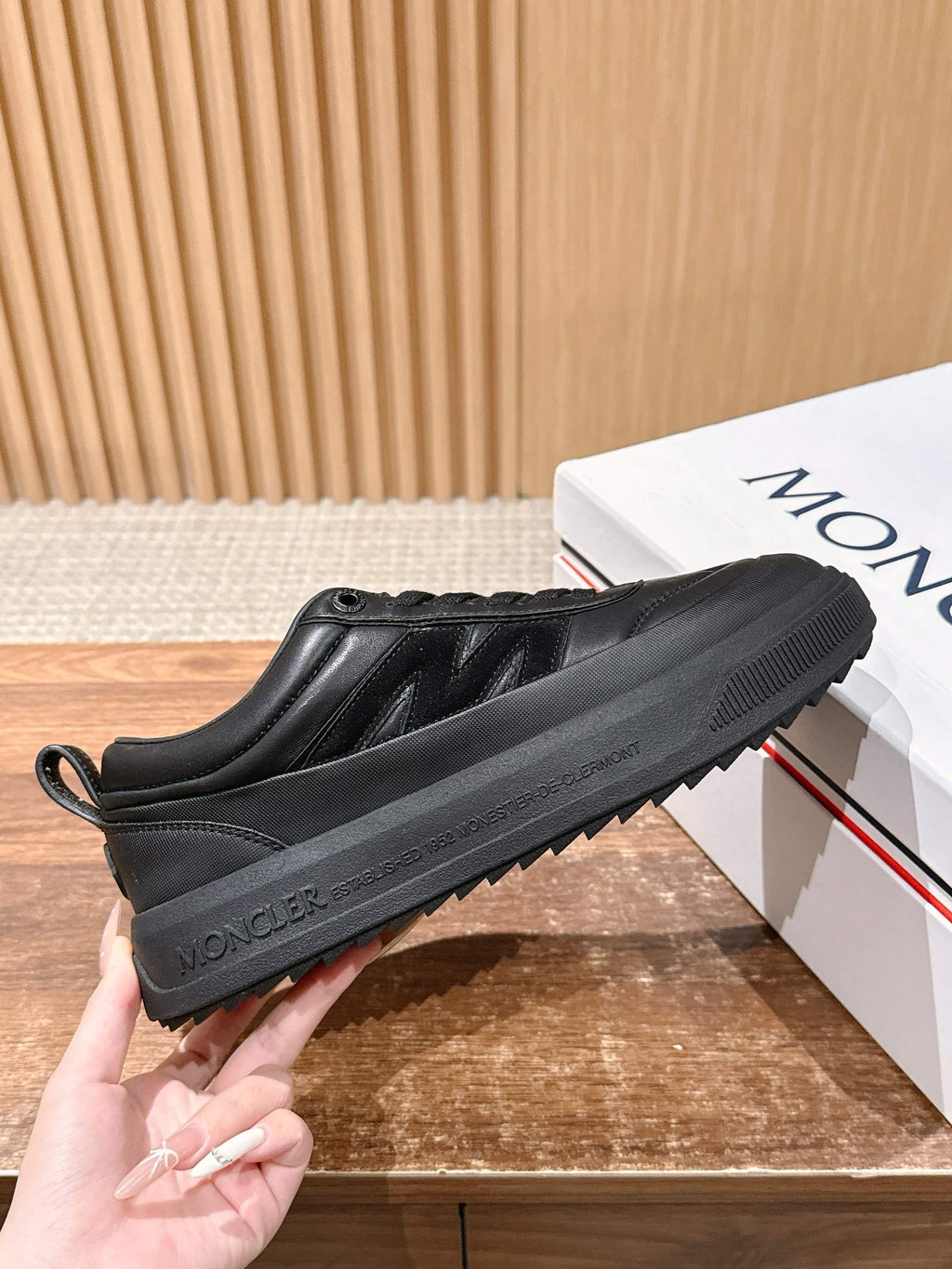 Black Moncler sneakers, side view, with textured sole and lace upper.