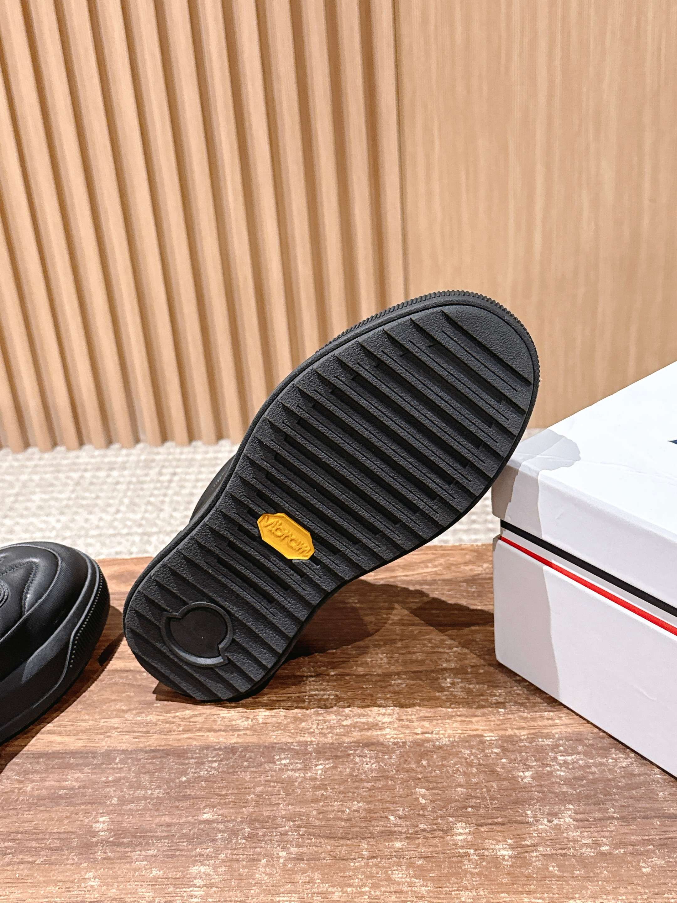 Black Moncler sneaker outsole with ribbed tread and small yellow accent.