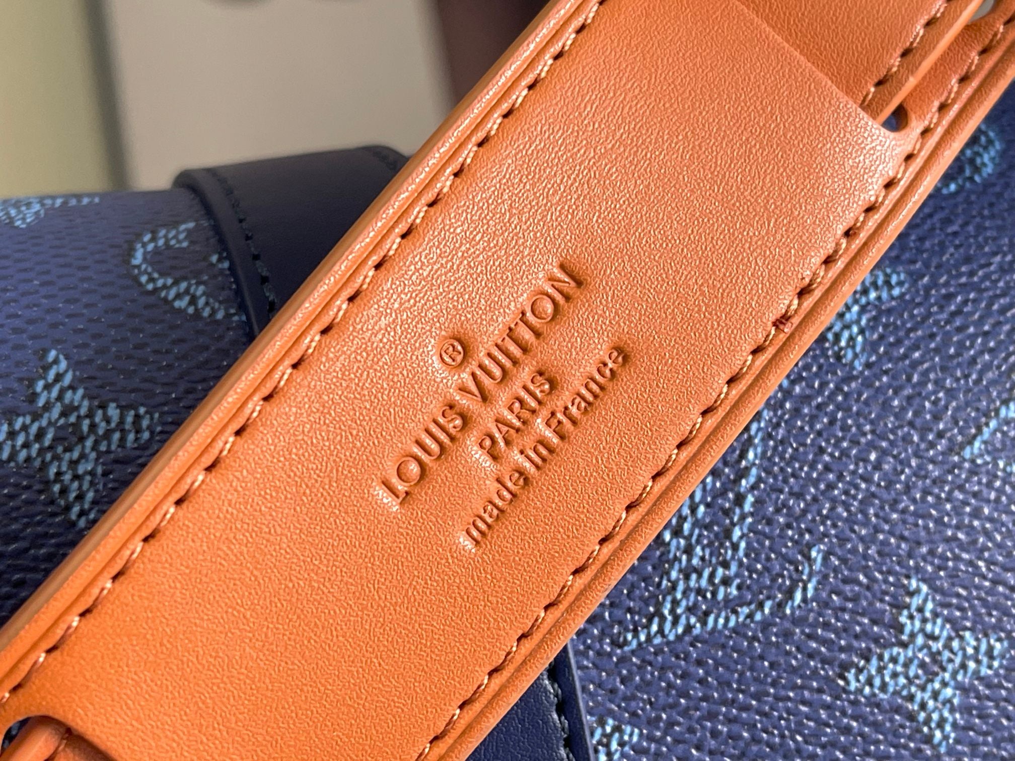 Louis Vuitton bag strap close-up in orange leather with embossed branding on tab