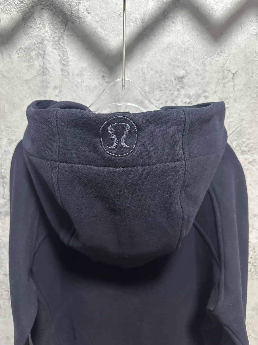 Dark zip-up hoodie back with hood and oval logo patch near neckline