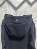 Dark zip-up hoodie back with hood and oval logo patch near neckline