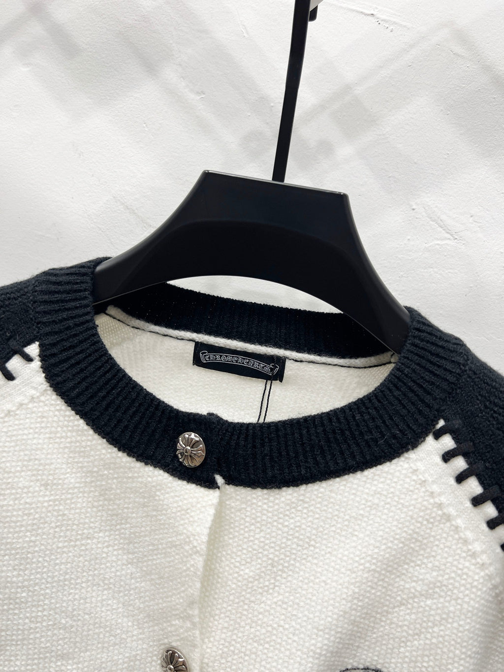White cardigan with navy ribbed crew neck and buttoned placket.
