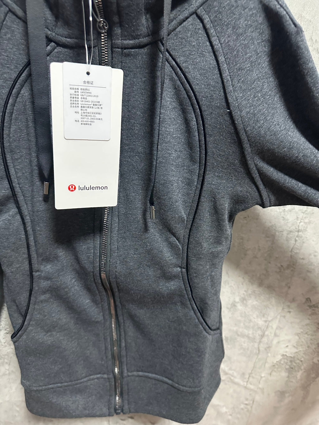 Dark gray zip-up hoodie front close-up with zipper, kangaroo pocket, and tags