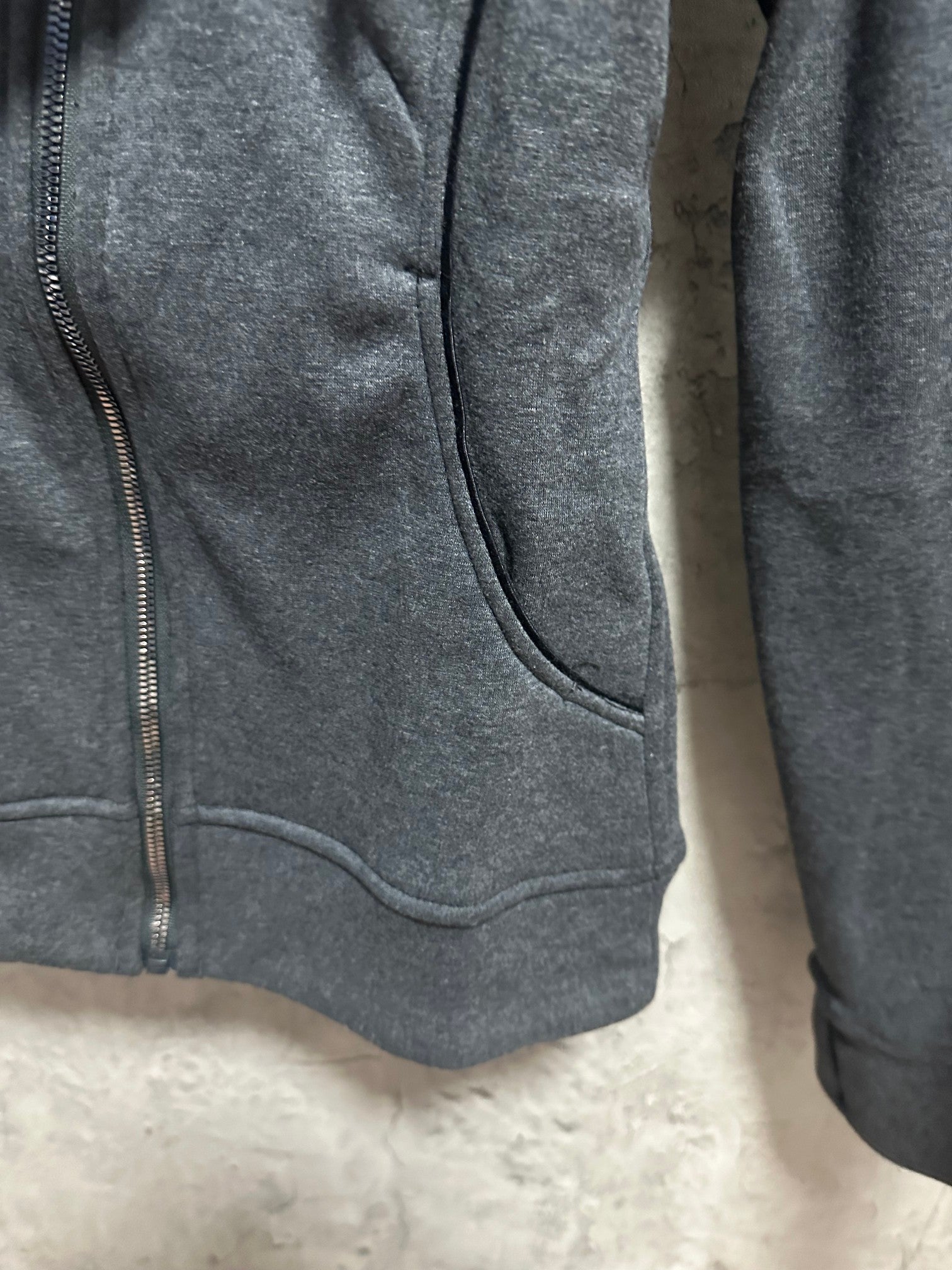 Dark gray zip-up hoodie sleeve and hem, showing front pocket opening