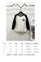 White and black raglan cardigan with button front and chest crest patch on display.