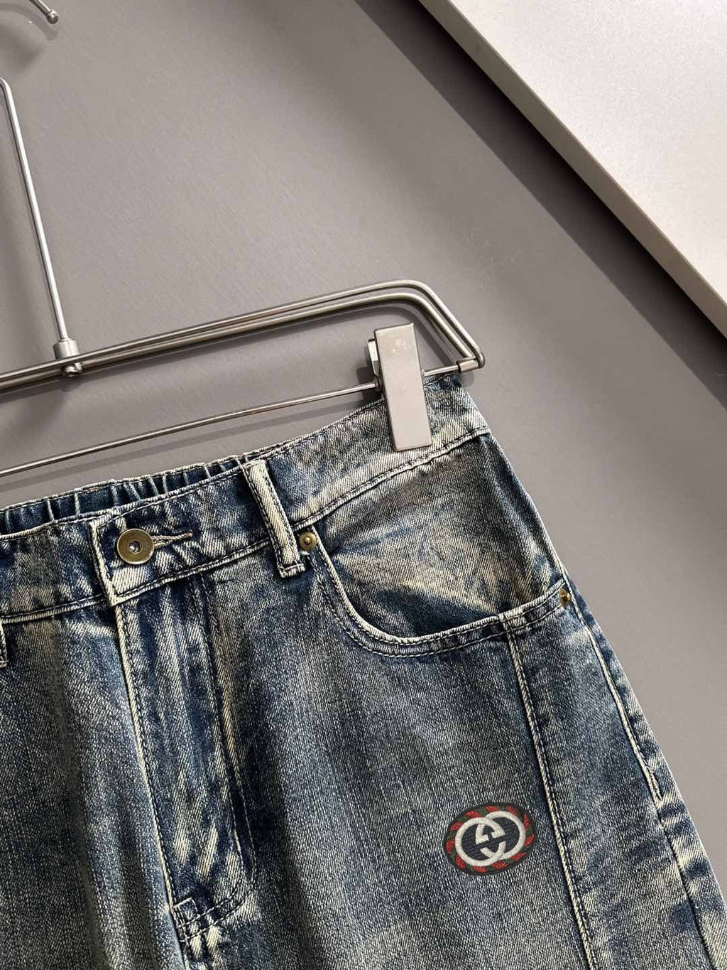 Denim pants waistband close-up with button, belt loops, and Gucci logo emblem