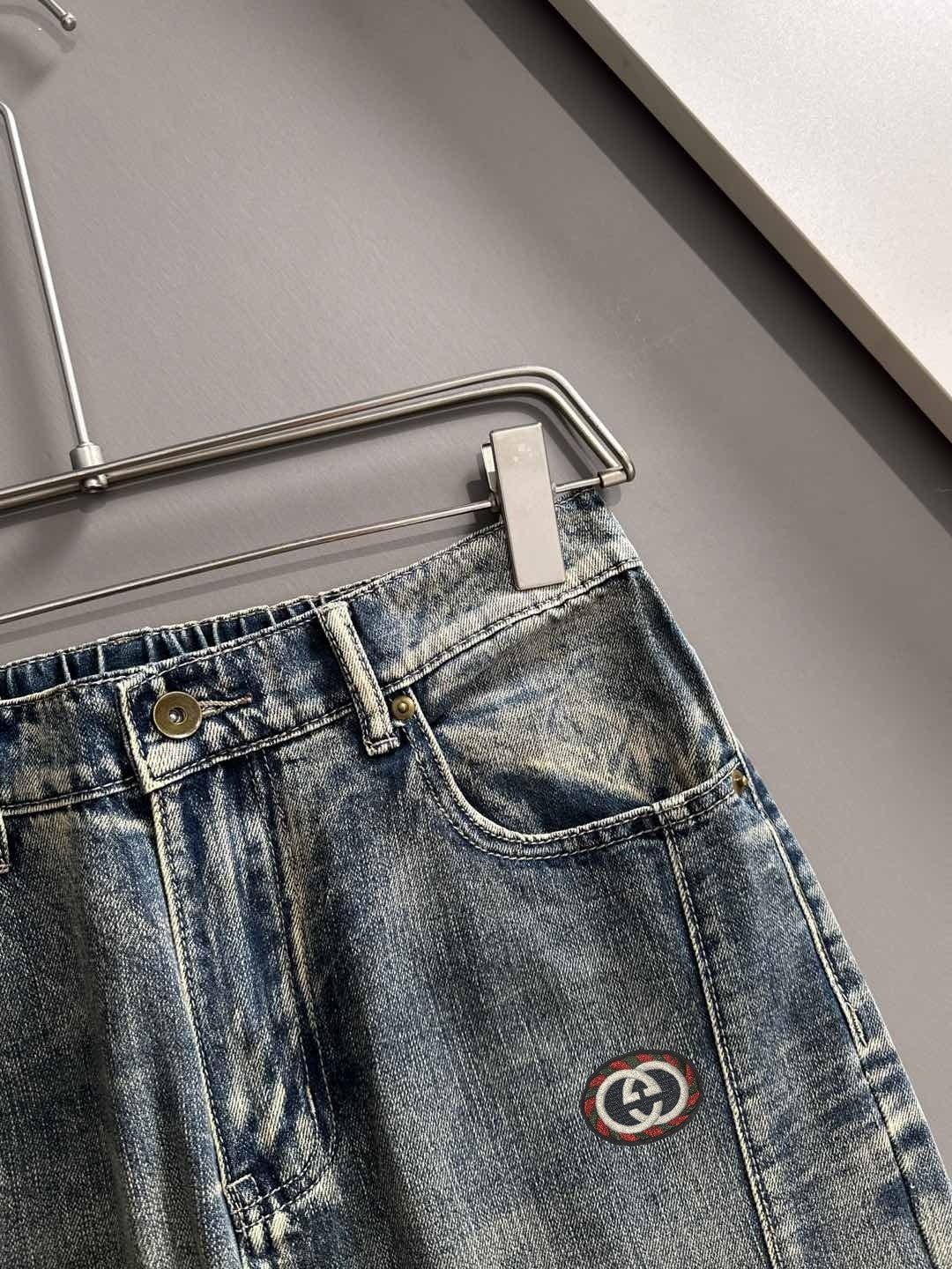 Denim pants waistband close-up with button, belt loops, and Gucci logo emblem