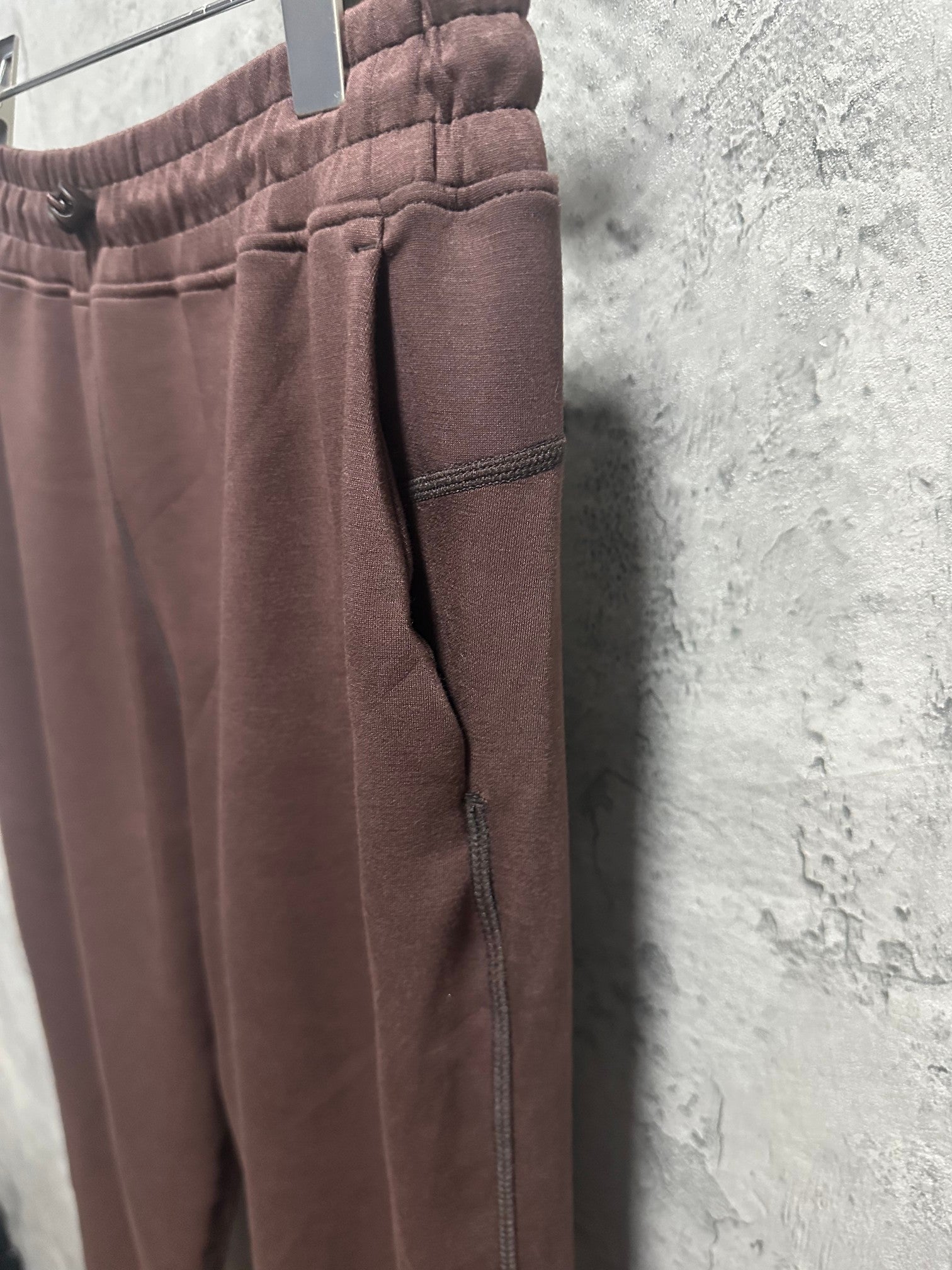Maroon sweatpants side view with tapered ankle hem and visible pocket seam