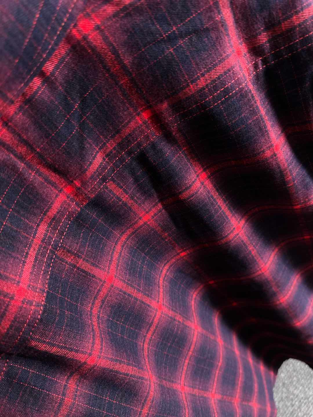 Long-sleeve plaid shirt fabric close-up, red grid pattern on dark base