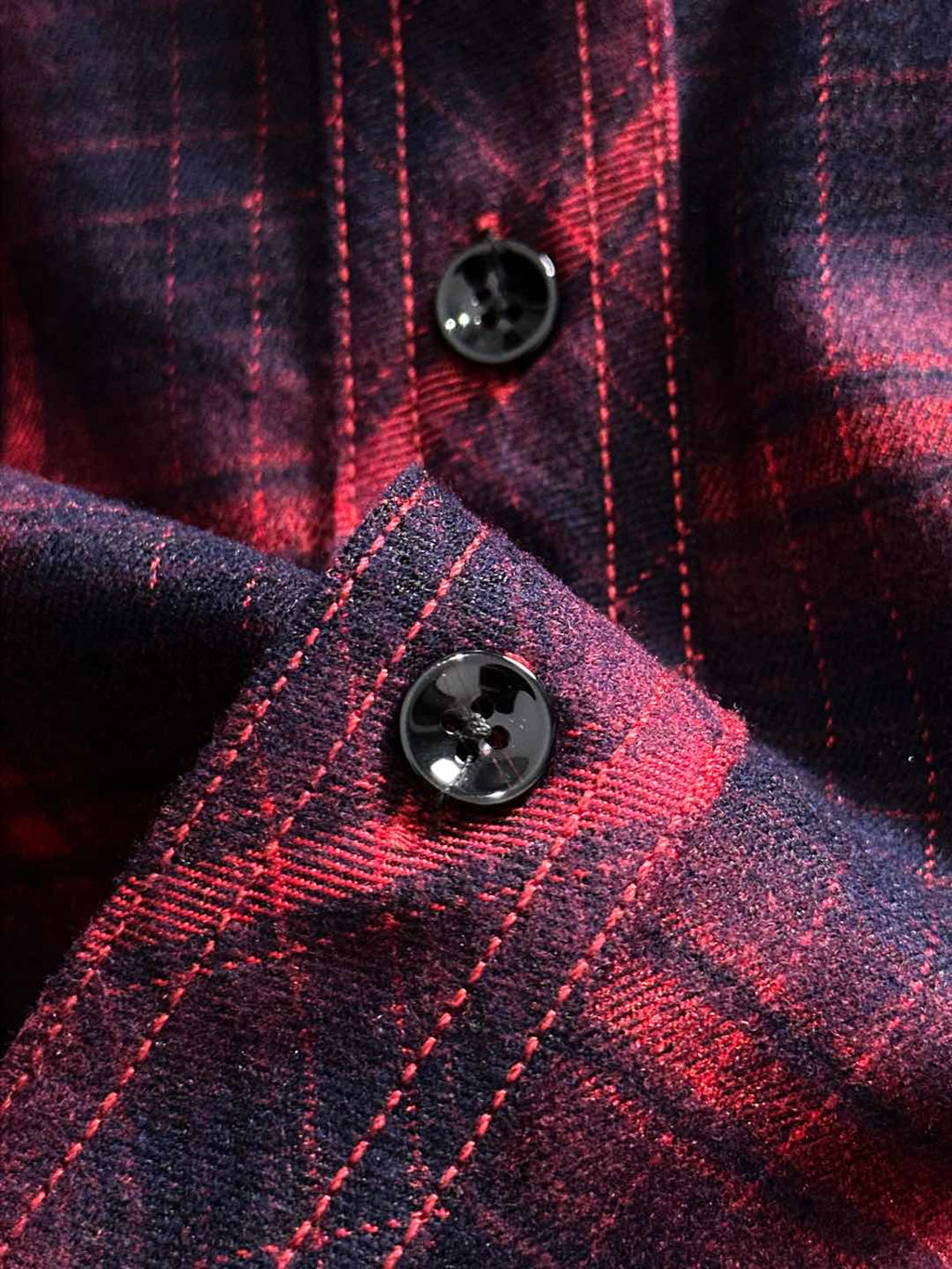 Long-sleeve plaid shirt button close-up, dark round buttons on red plaid
