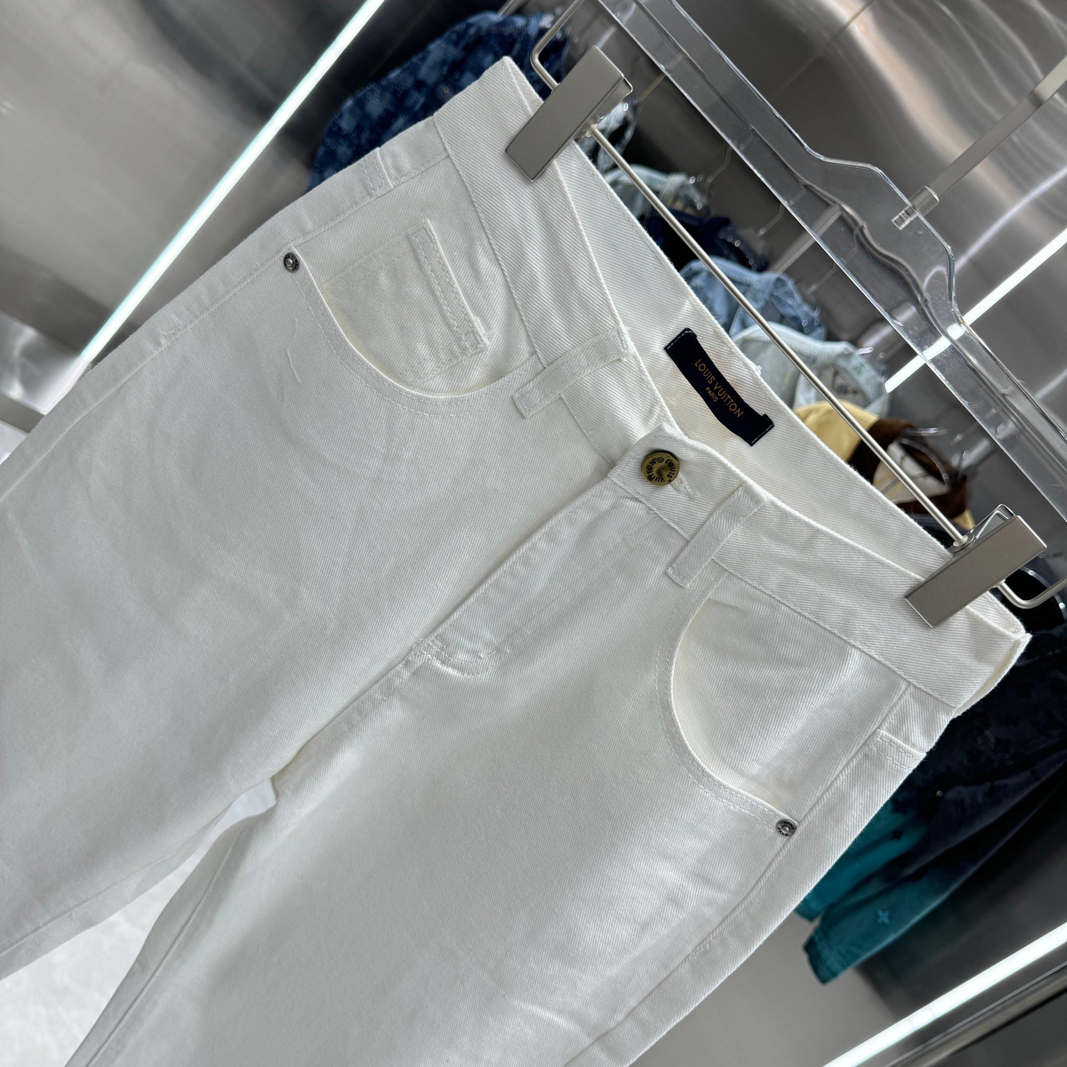 White denim pants with curved front pockets and gold-tone button at waistband