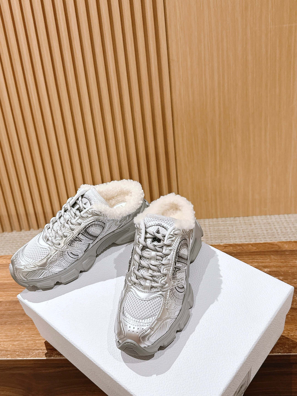 Silver metallic lace-up sneakers with fuzzy lining and star logo, side-by-side on box