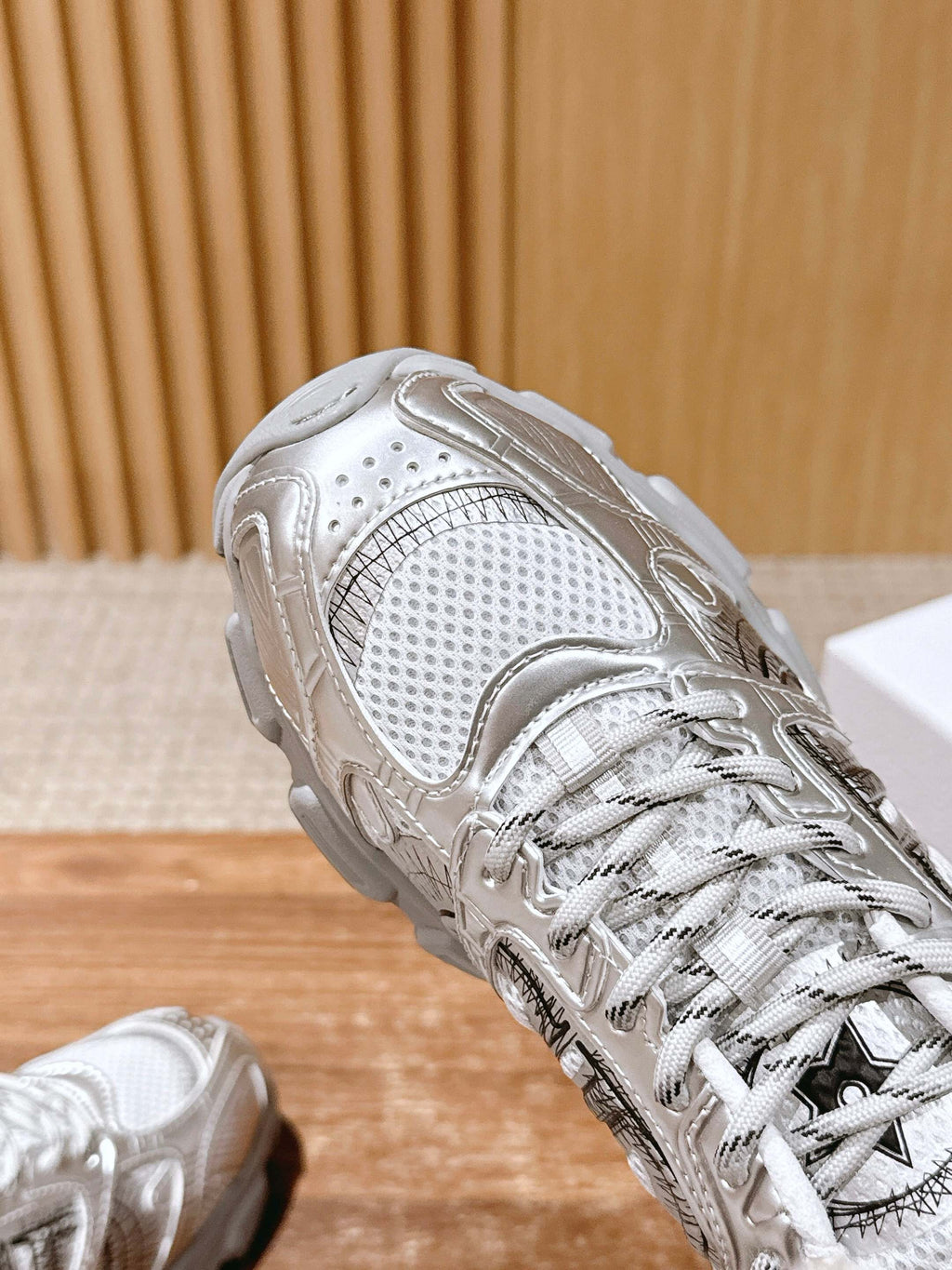 Close-up of metallic silver sneaker upper with woven pattern and lace detail.