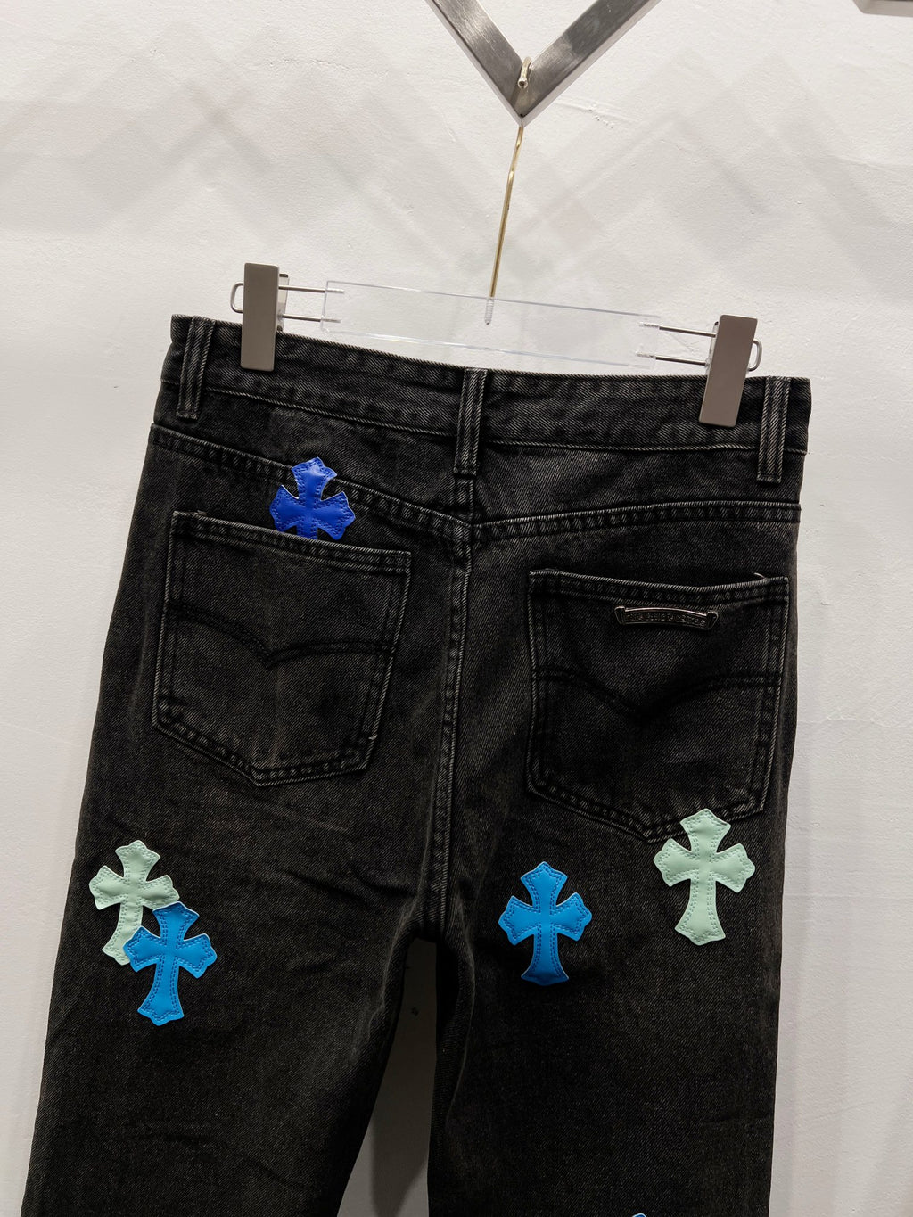 Black denim pants with cross-style patches on the lower back leg