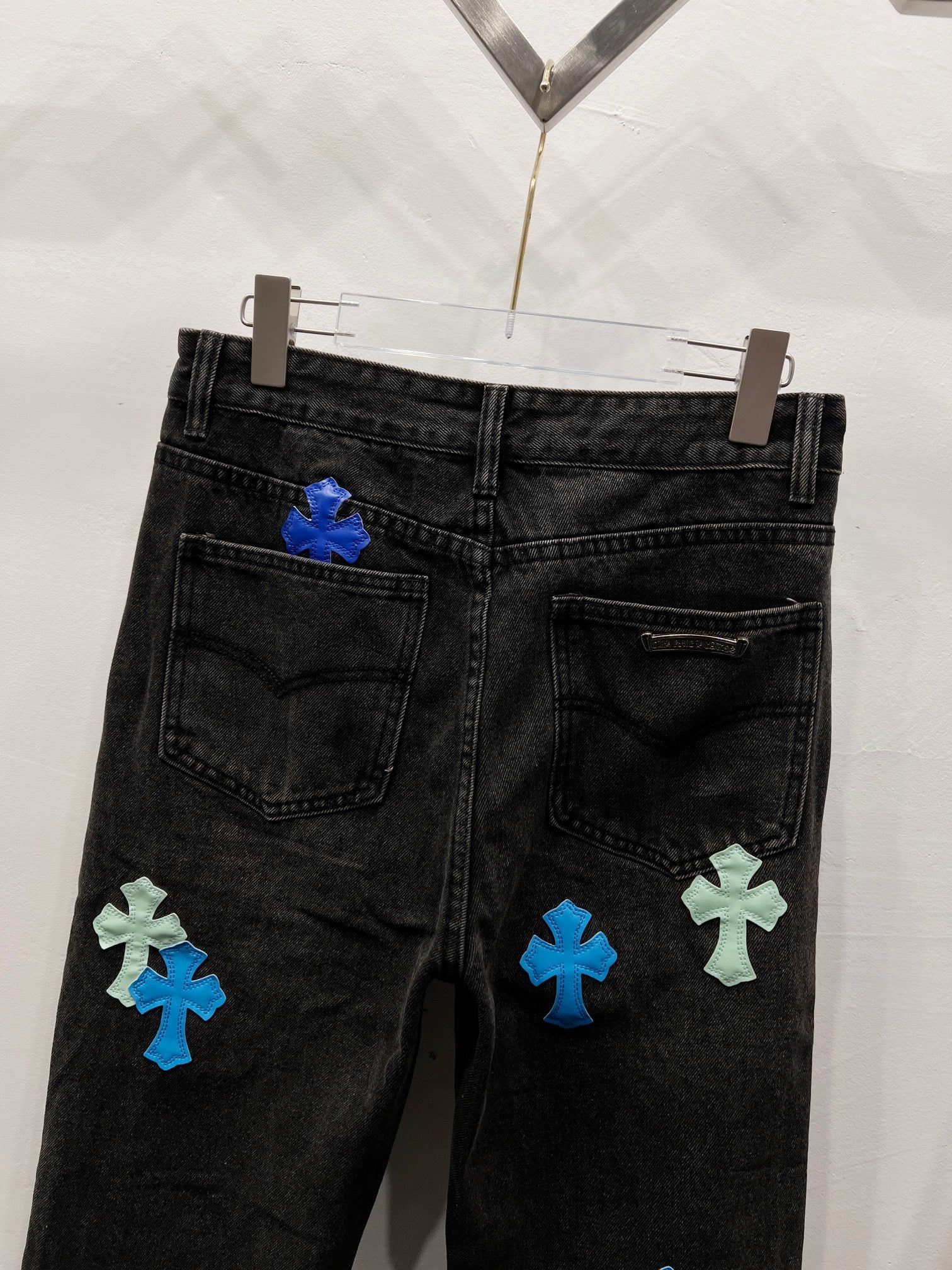 Black denim pants with cross-style patches on the lower back leg