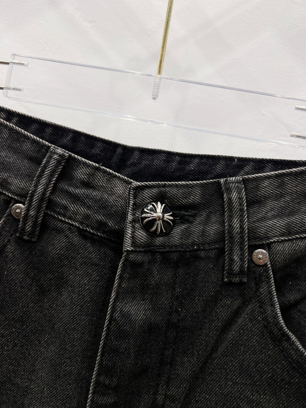 Black denim pants waistband with decorative stitched emblem on belt area