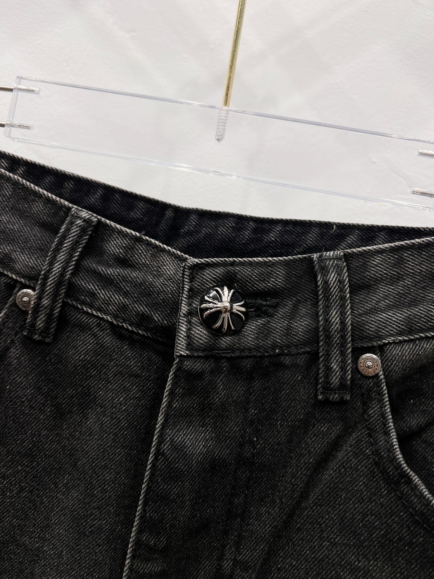 Black denim pants waistband with decorative stitched emblem on belt area