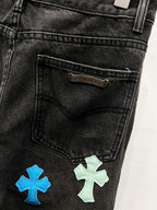 Black denim pants with stitched label and cross patches near right pocket