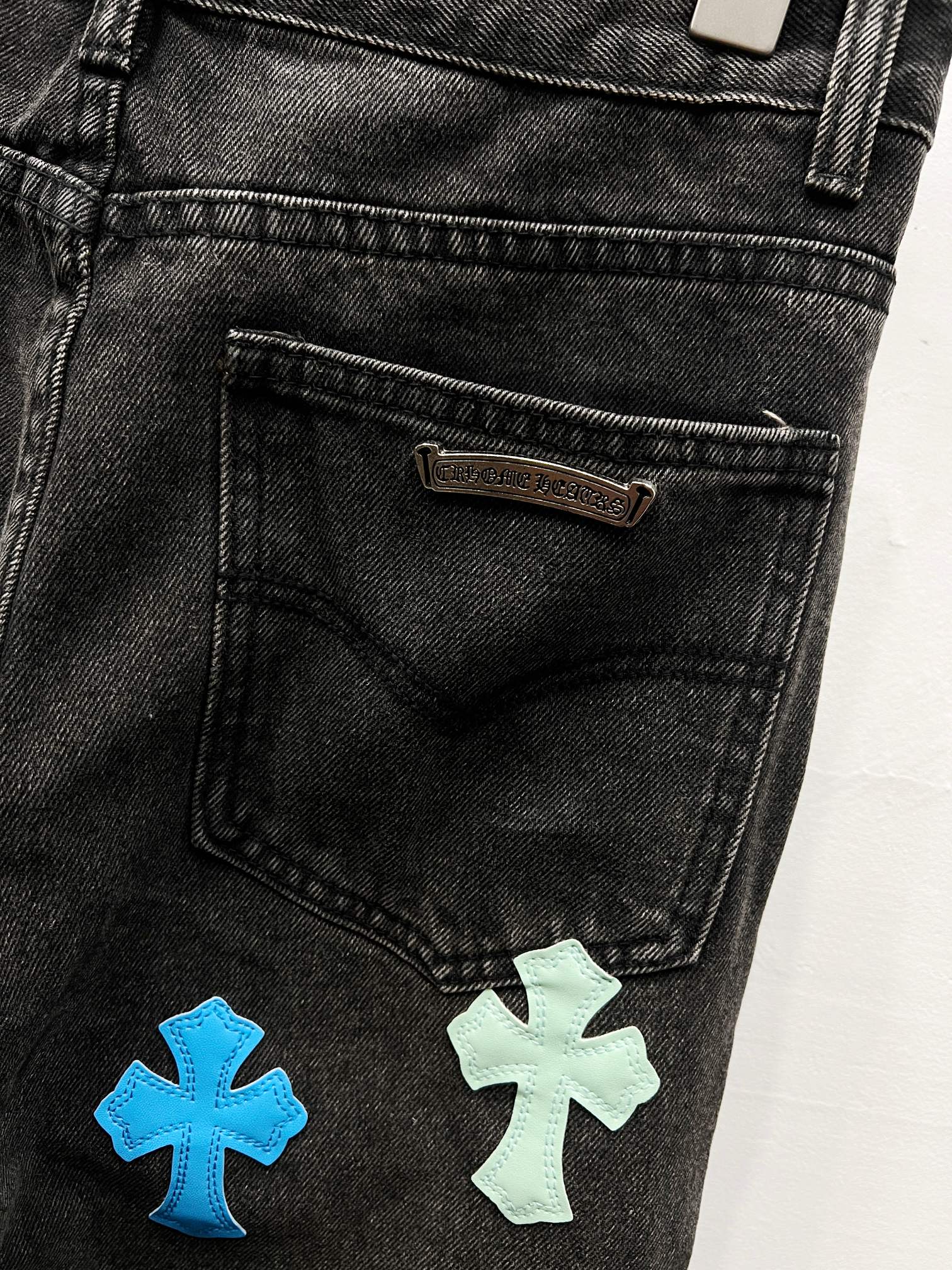 Black denim pants with stitched label and cross patches near right pocket