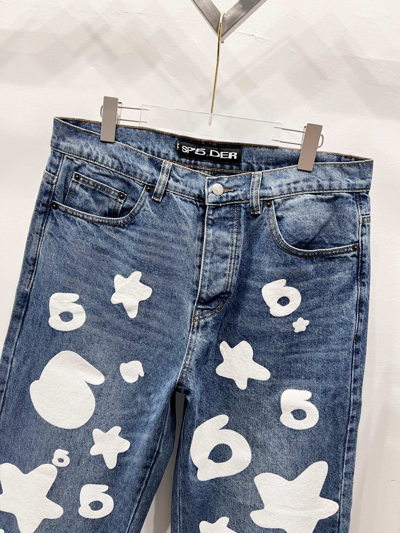 Blue denim pants with white graphic patches, close-up front pockets