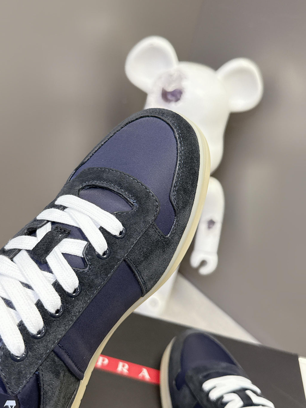 Prada unisex sneaker side view, navy suede upper with white laces and cream sole