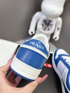 Blue and white Prada sneakers with heel branding, held in hand.