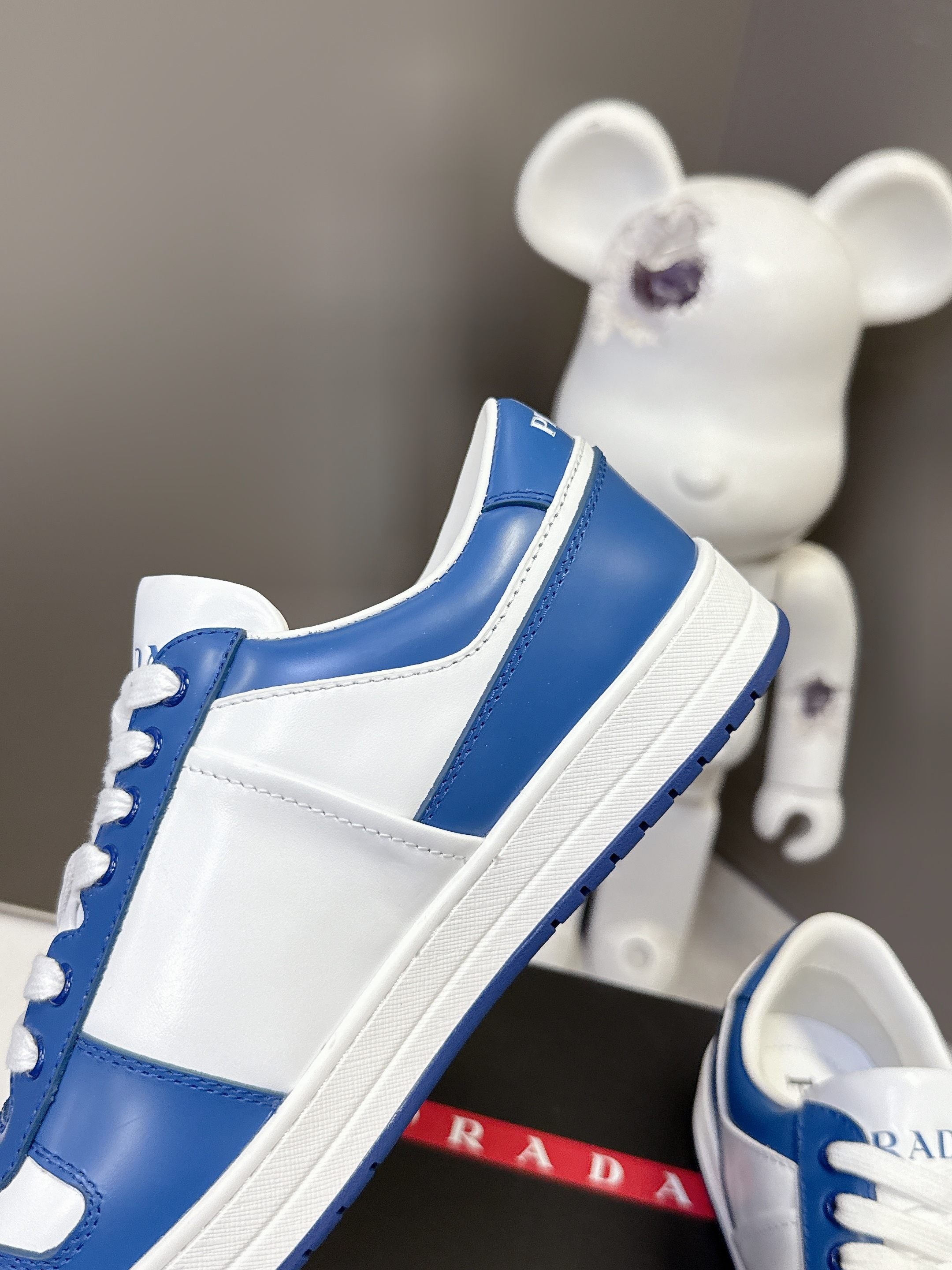 Blue and white Prada sneaker side view on black box.