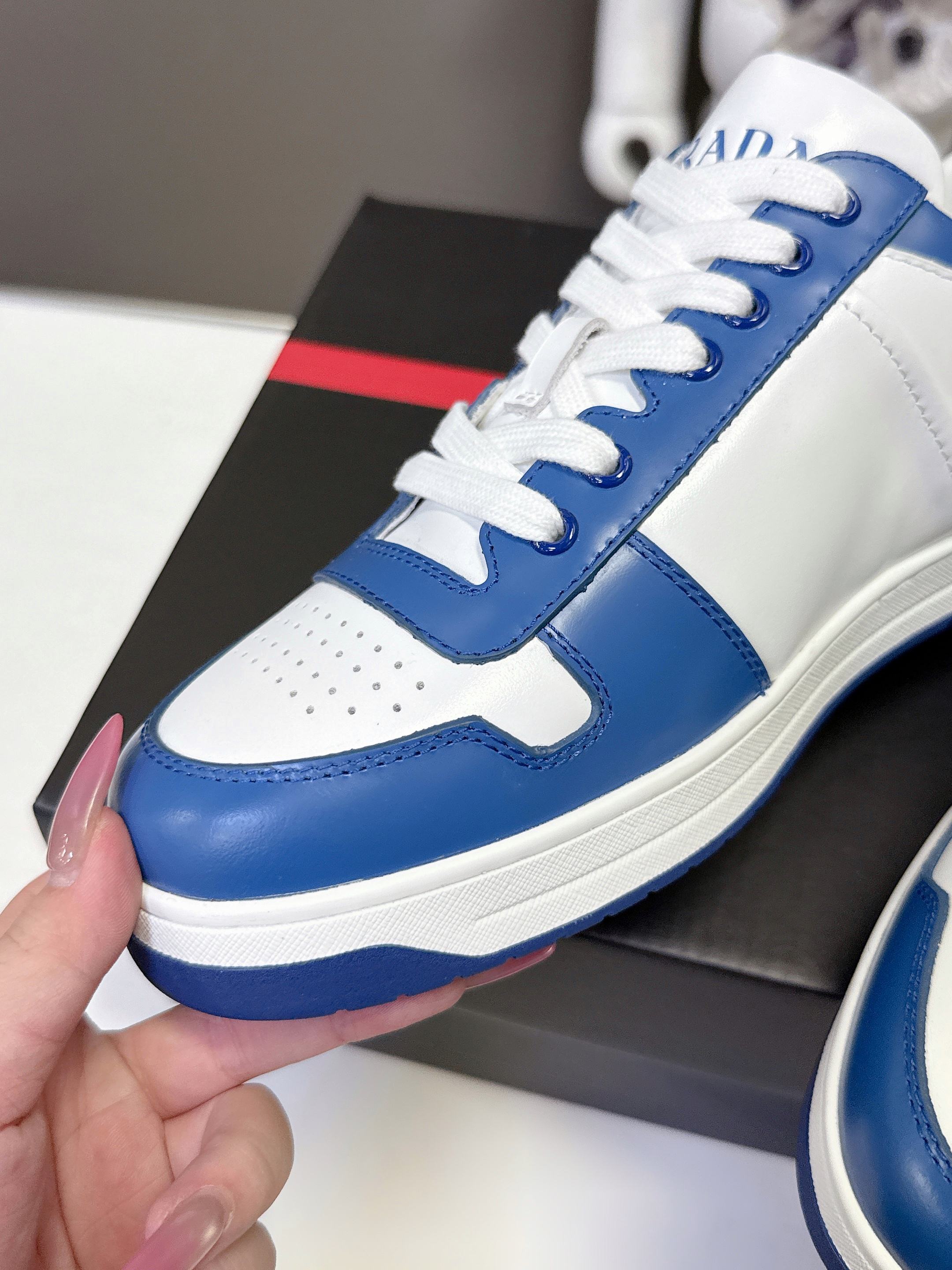 Blue and white Prada low-top sneaker with white laces, close-up on box.