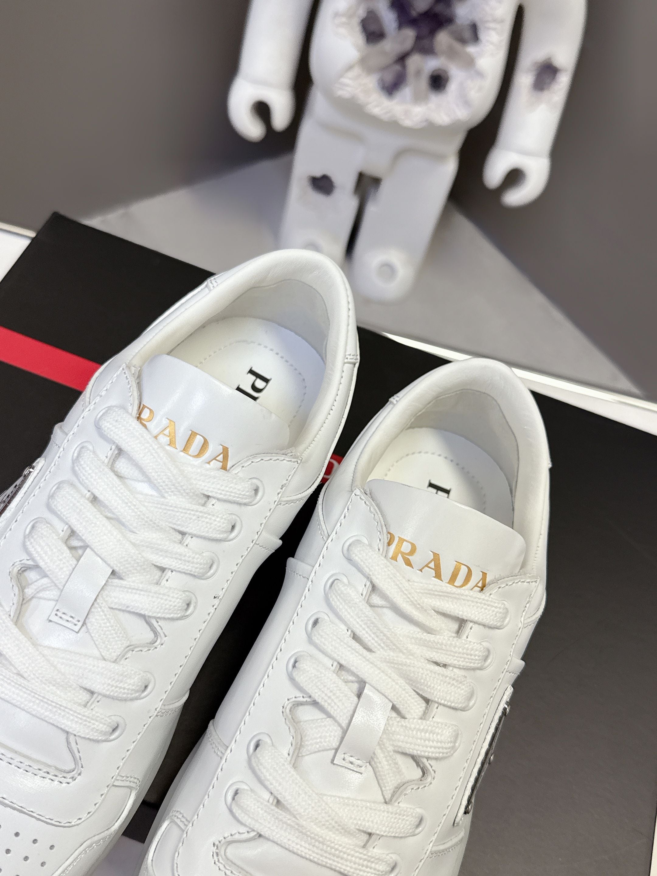 White Prada sneakers close-up of tongue with gold logo on black box