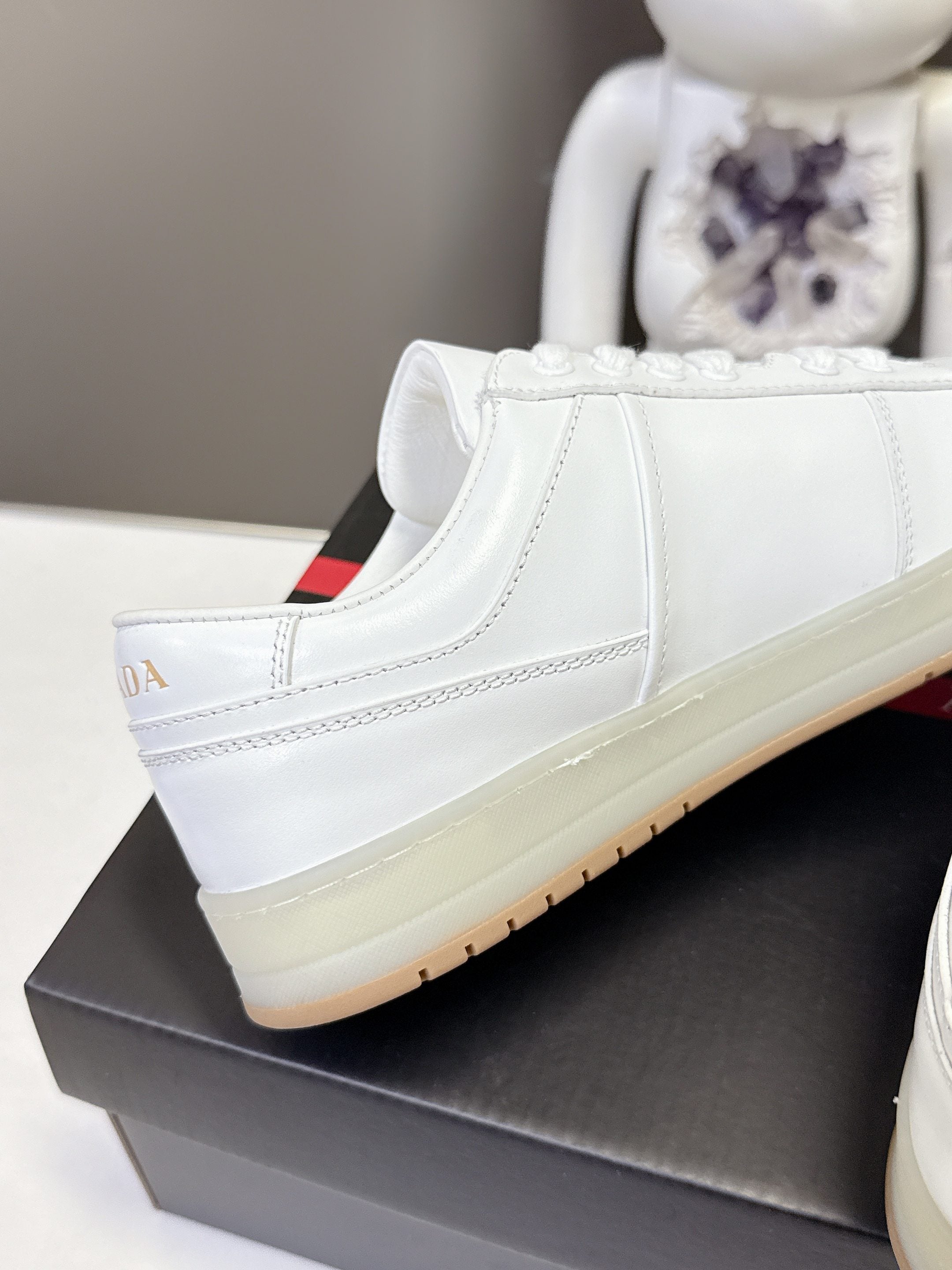 White Prada low-top sneaker side profile with off-white sole on black box