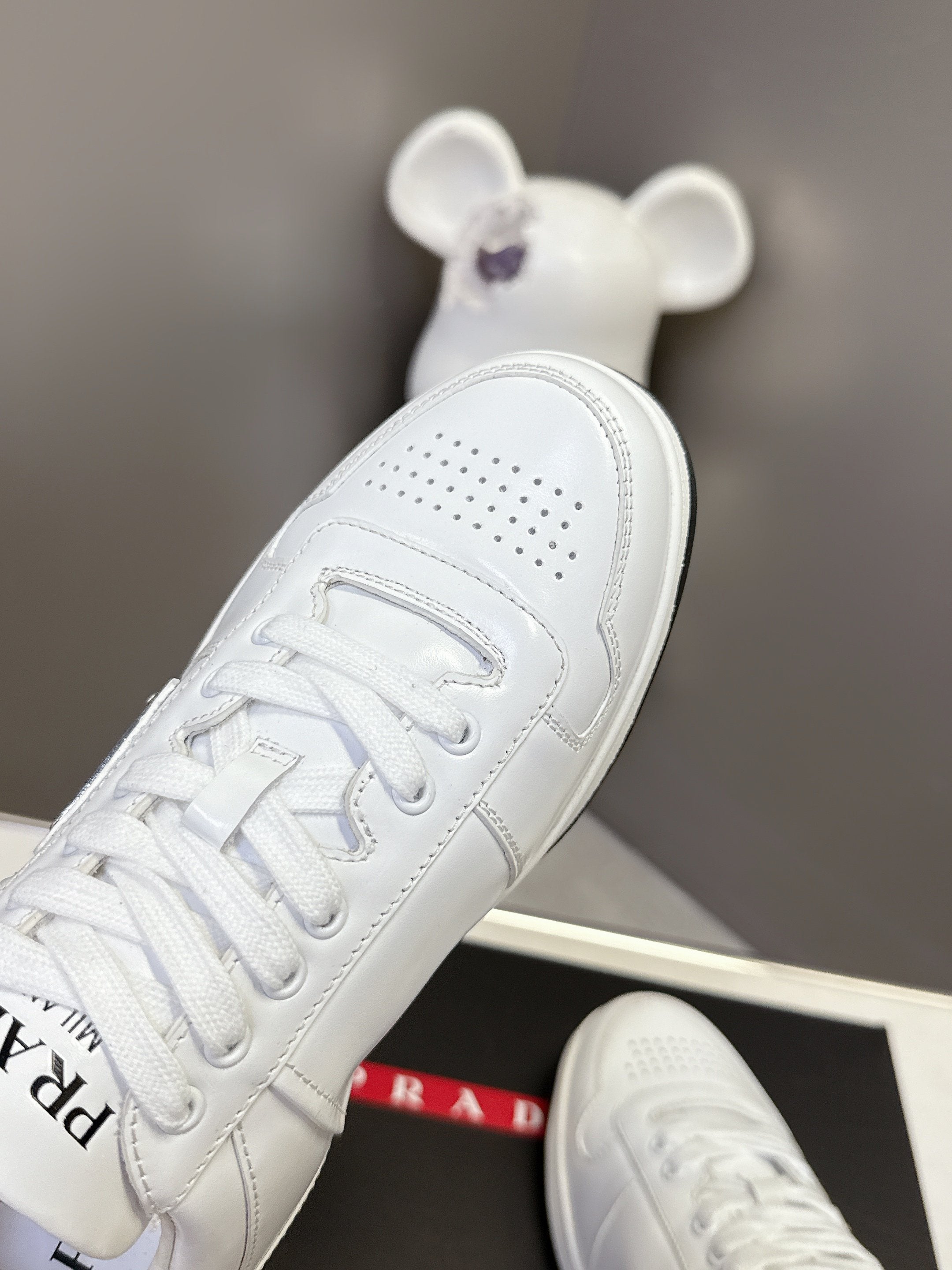 White Prada unisex sneaker angled view with perforated toe and lace-up closure