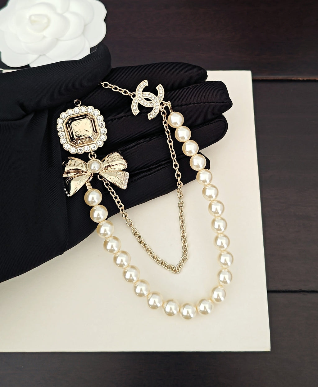 Gold-tone pearl necklace with square charm and bow accents on chain