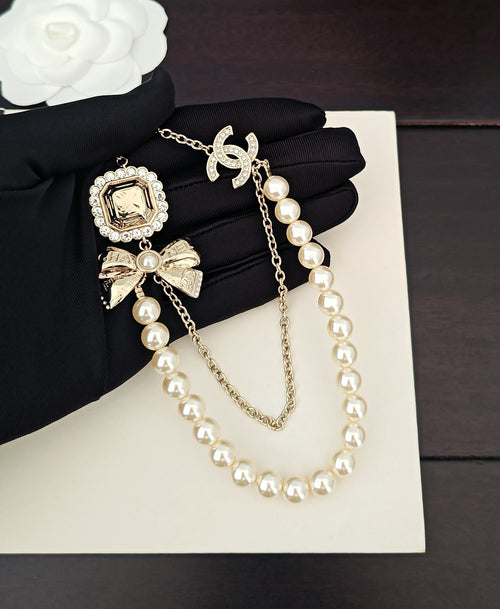 Gold-tone pearl necklace with square charm and bow accents on chain