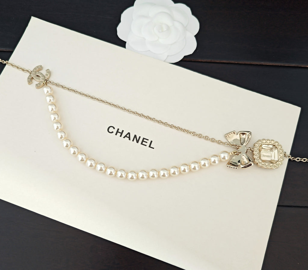 Gold-tone pearl necklace with bow and charm pendants on chain