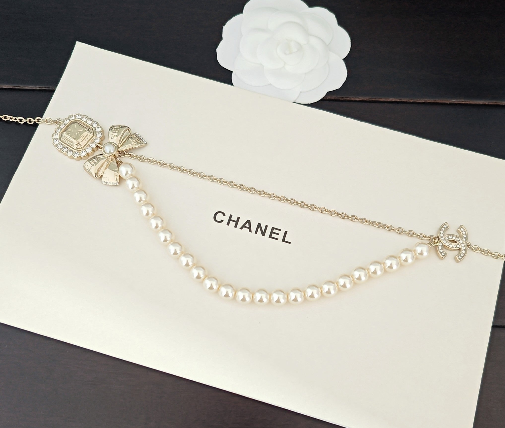 Gold-tone pearl necklace with square medallion, bow charm, and hanging pearls