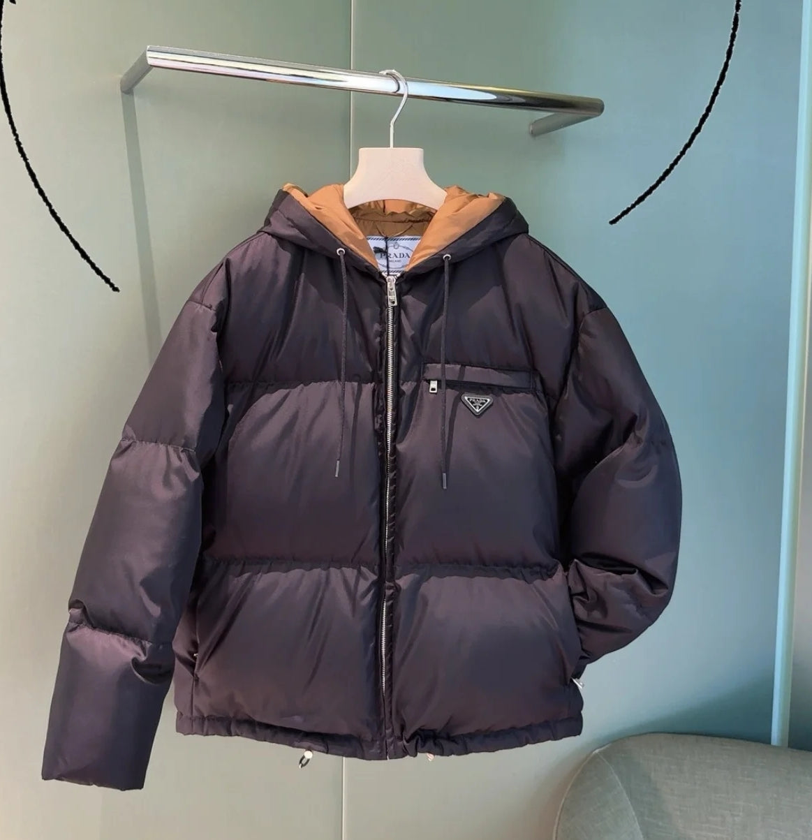 Prada hooded puffer jacket in dark color, full-zip front, logo patch on chest.