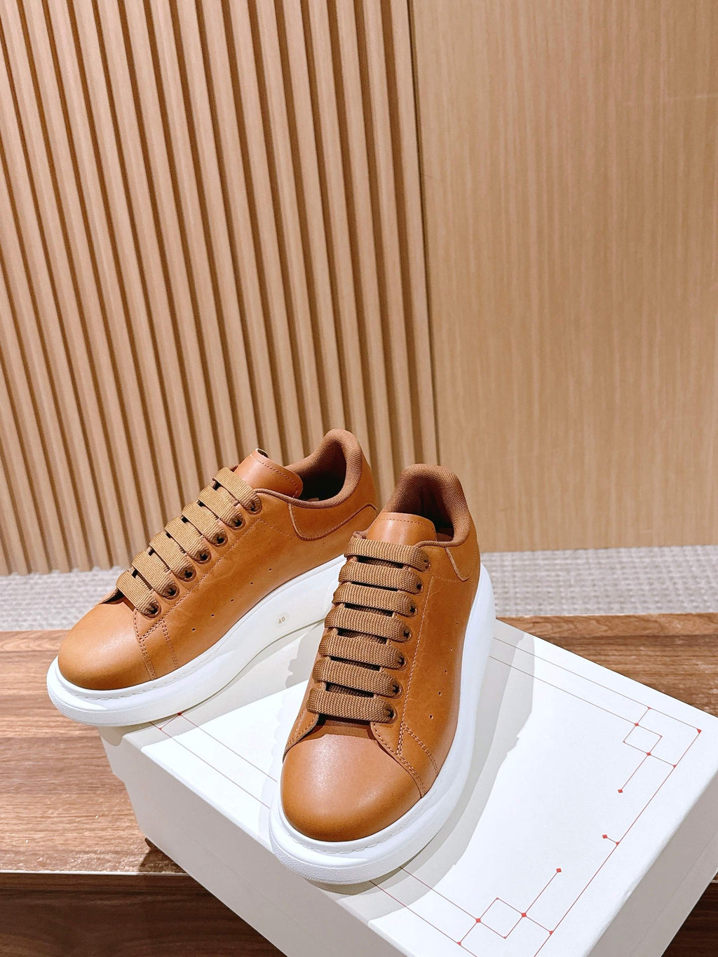 Tan leather low-top sneakers with wide laces and white rubber soles, side view