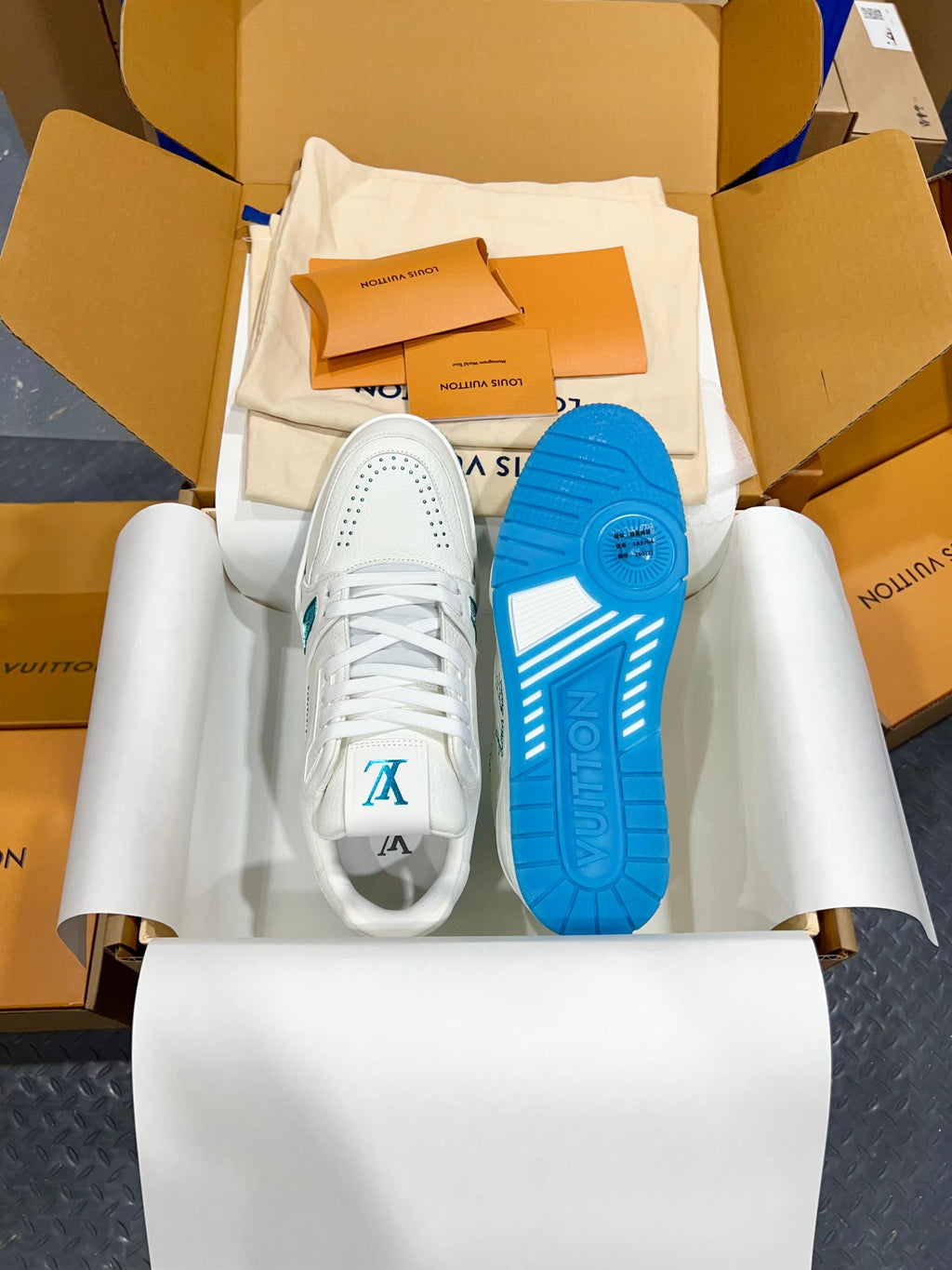 White Louis Vuitton trainer sneakers with blue outsole bottoms, pair in open box.