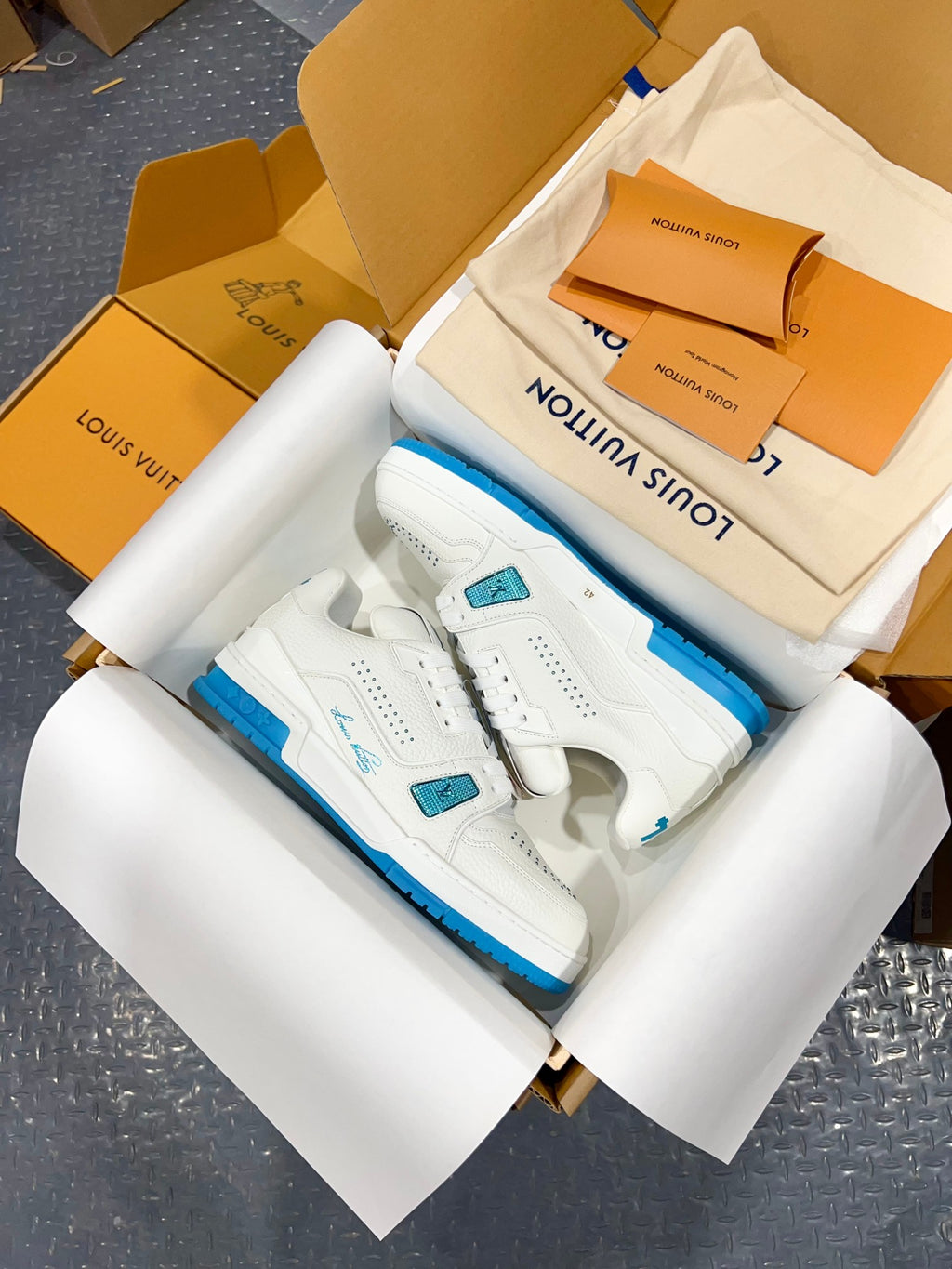 White Louis Vuitton trainer sneakers with blue sole edge and lace tab detail.