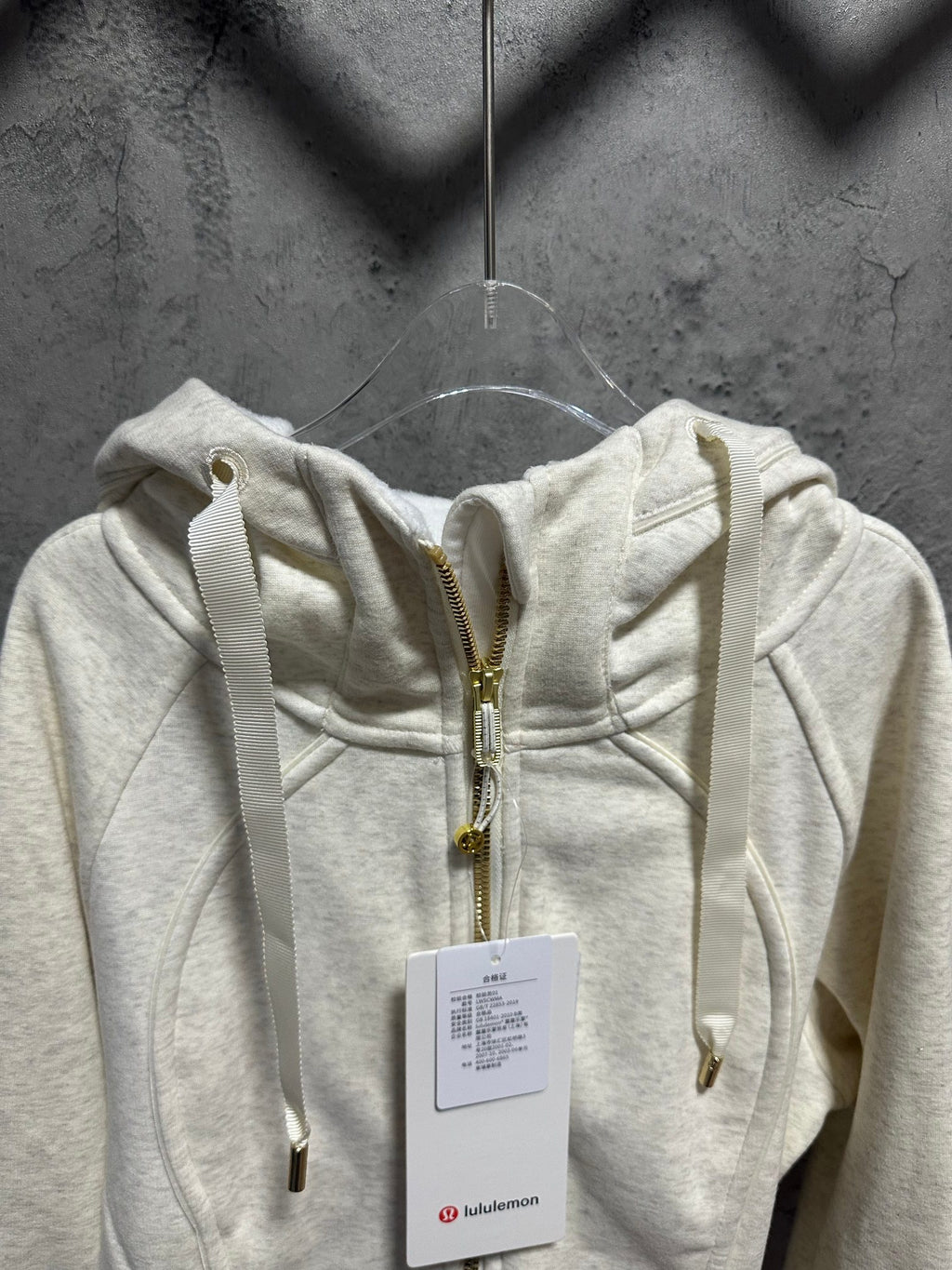 Cream zip-up hoodie with hood, gold zipper, and drawstring pulls